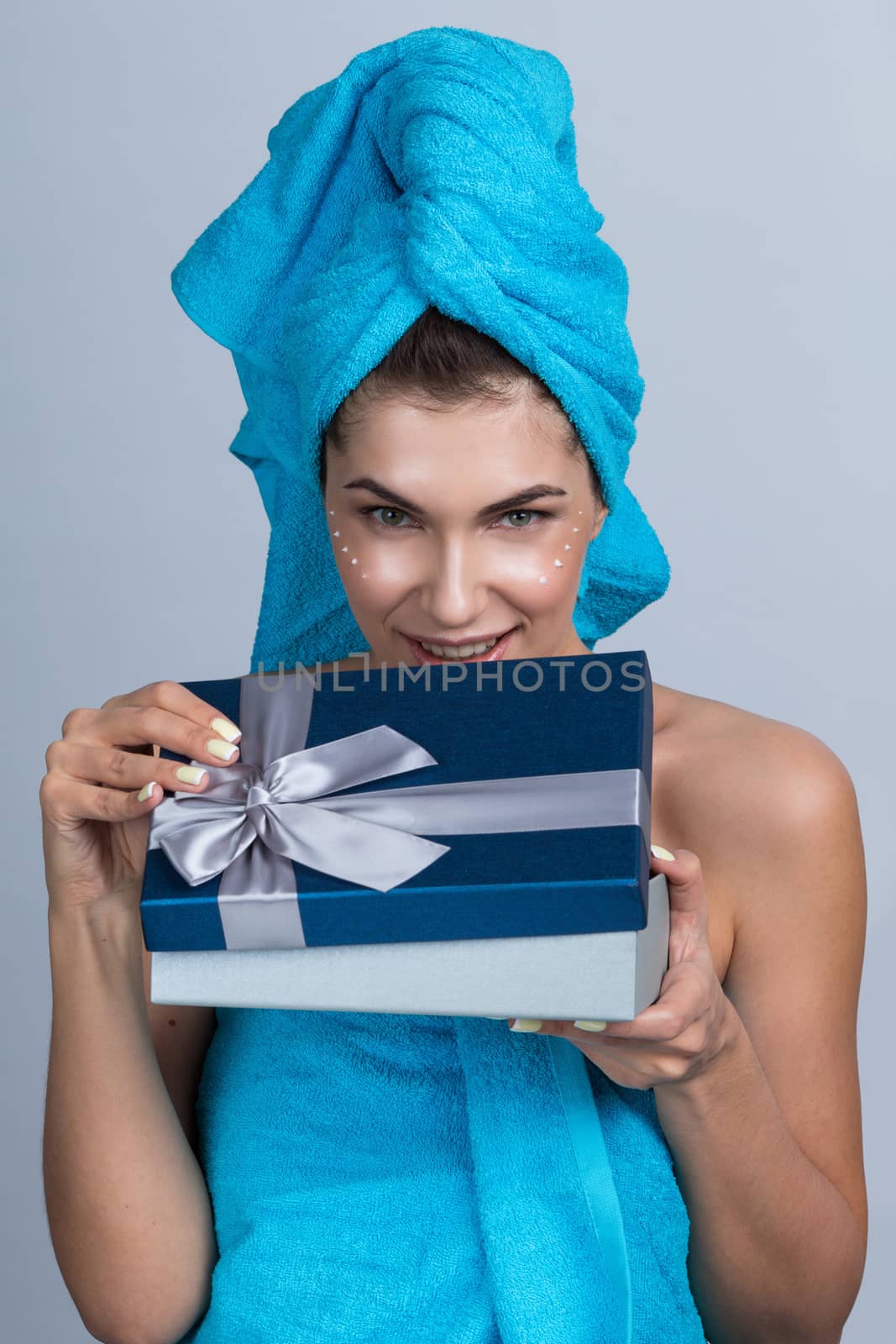 Beautiful young woman after shower with towel on head and creme on her face open beauty holiday gift