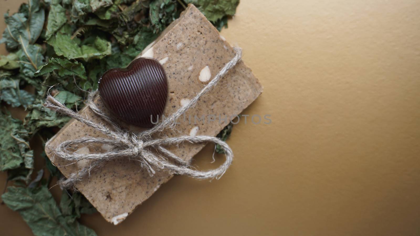 Organic handmade soap made of field herbs. Soap in a rope with dry grass and chocolate candy on a golden background