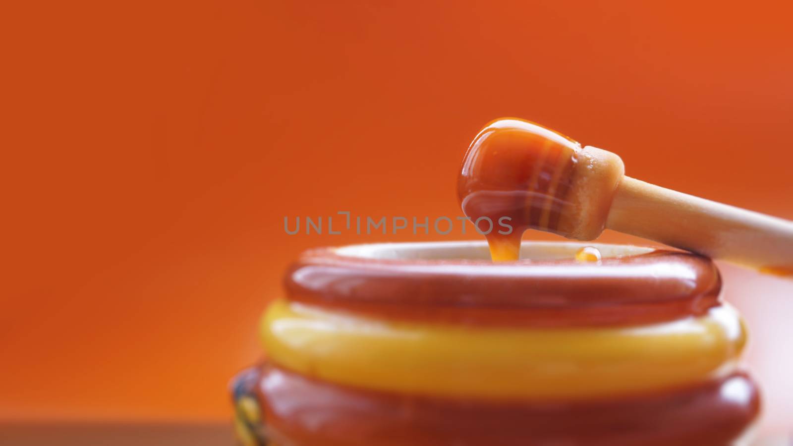 Honey dripping from honey dipper on yellow background. Thick honey dipping from the wooden honey spoon. Healthy food concept, diet, dieting