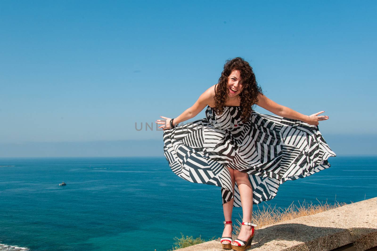 Portrait of a laughing girl in a light dress against the blue sea on a warm summer day