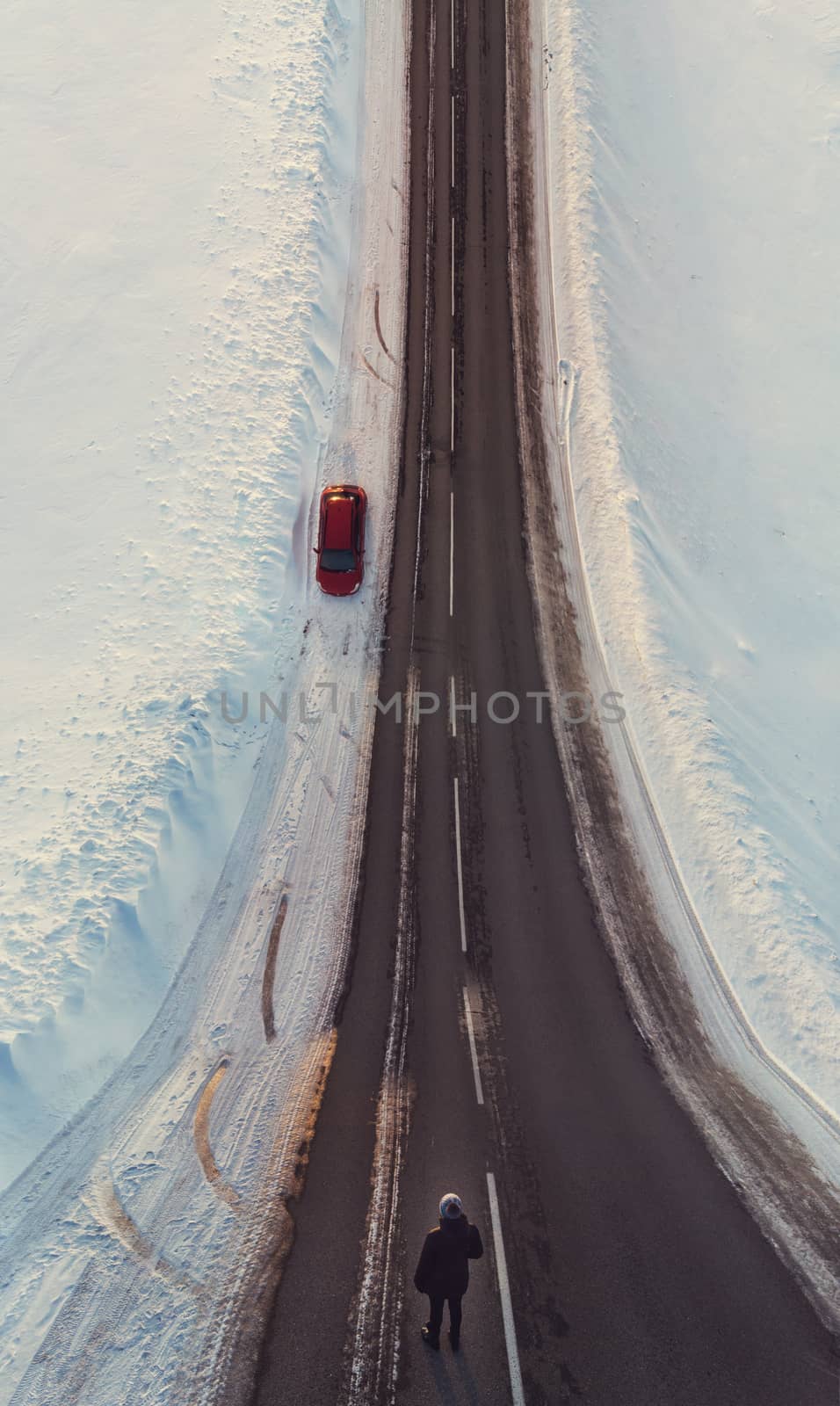 Surreal image with an unusual perspective with a woman on a winter road and car, simultaneous top view and normal view