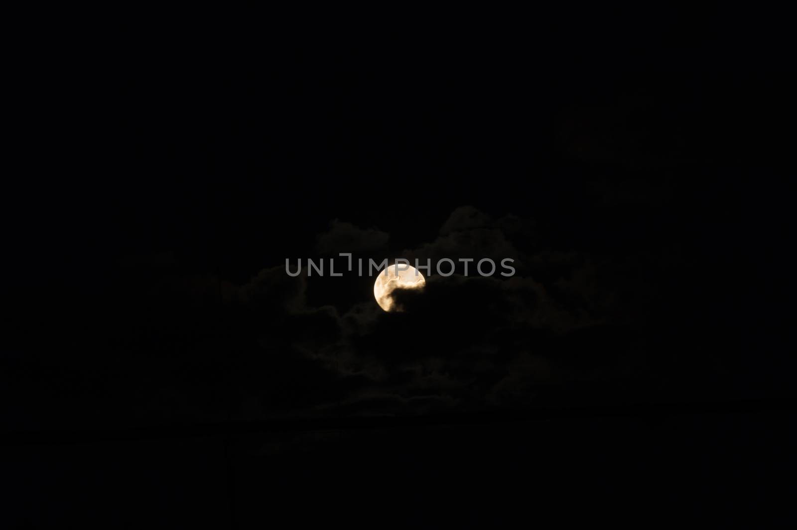 The moon behind clouds over a dark sky