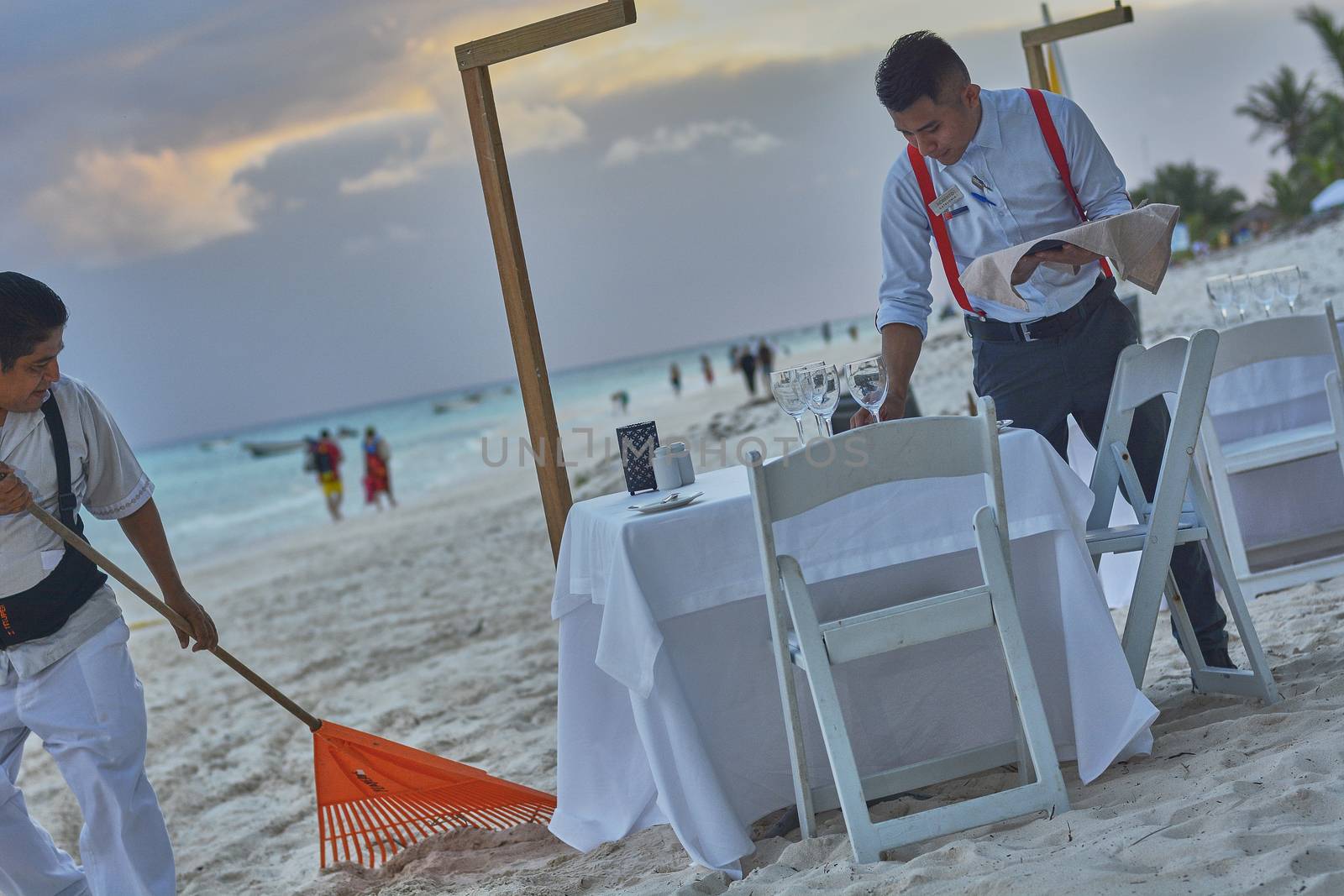 Well-dressed waiter intent on setting a table on the beach of Xpu-Ha in Mexico for a dinner by the sea