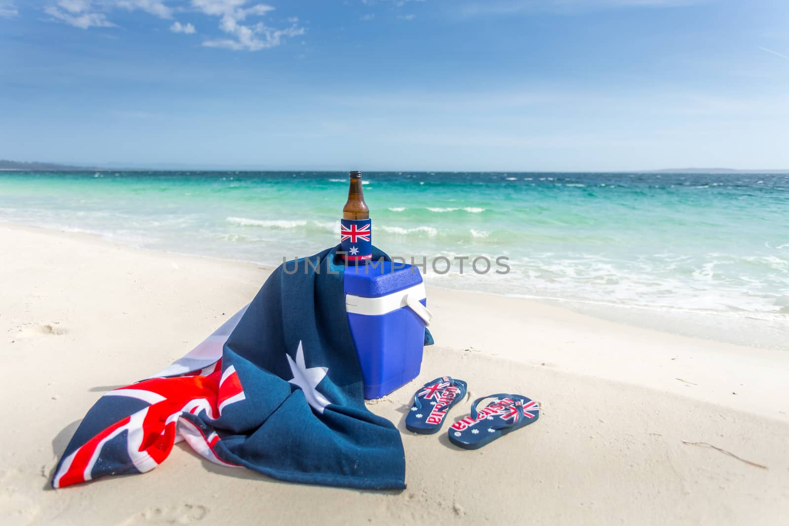Iconic Australian items on a beach, esky, beach towel, beer or beverage and thongs.  Some items have the Australian flag on them