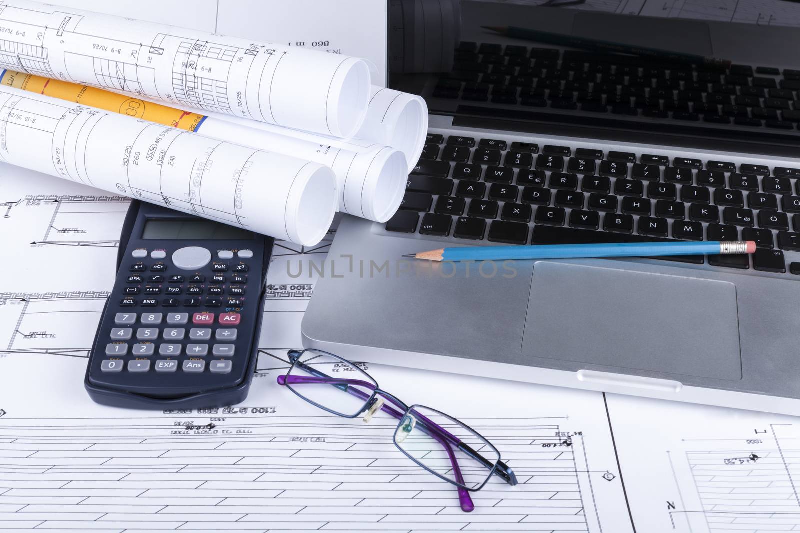 Architect blueprints with a calculator ans a silver laptop with pencil and glasses