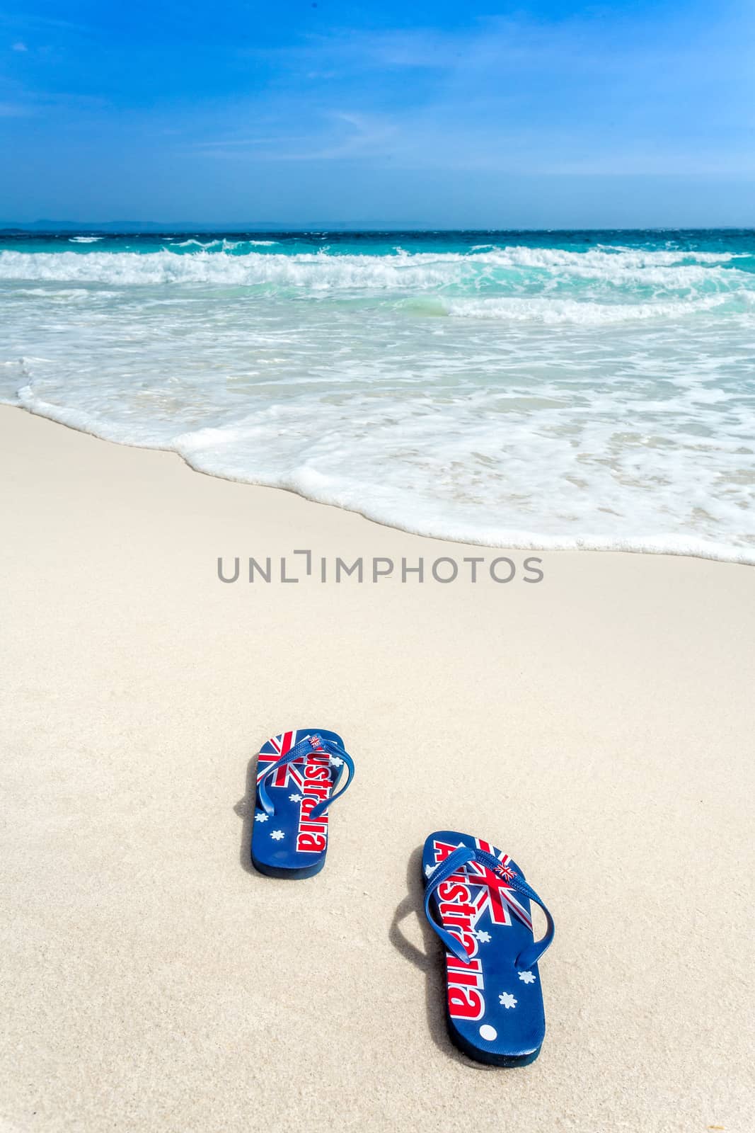 Australian flag printed on thongs on the beachwith an encrouching wave coming toward them  in summer sun