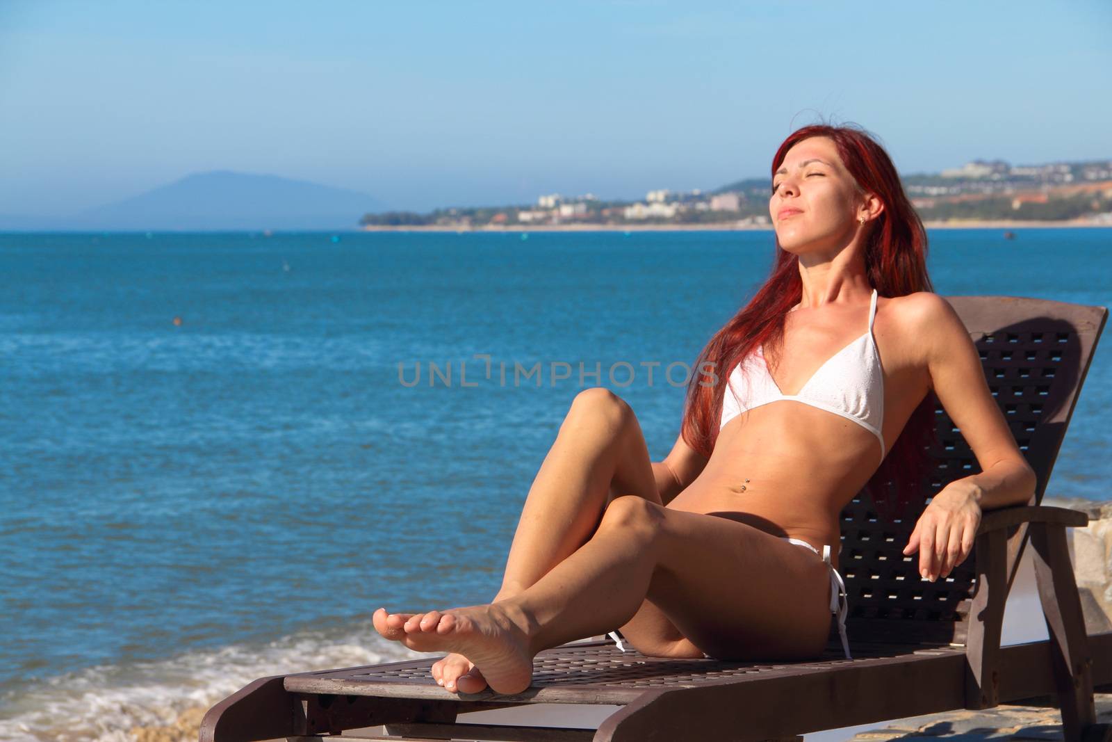 Happy young woman in bikini rest on sea beach on chaise lounge