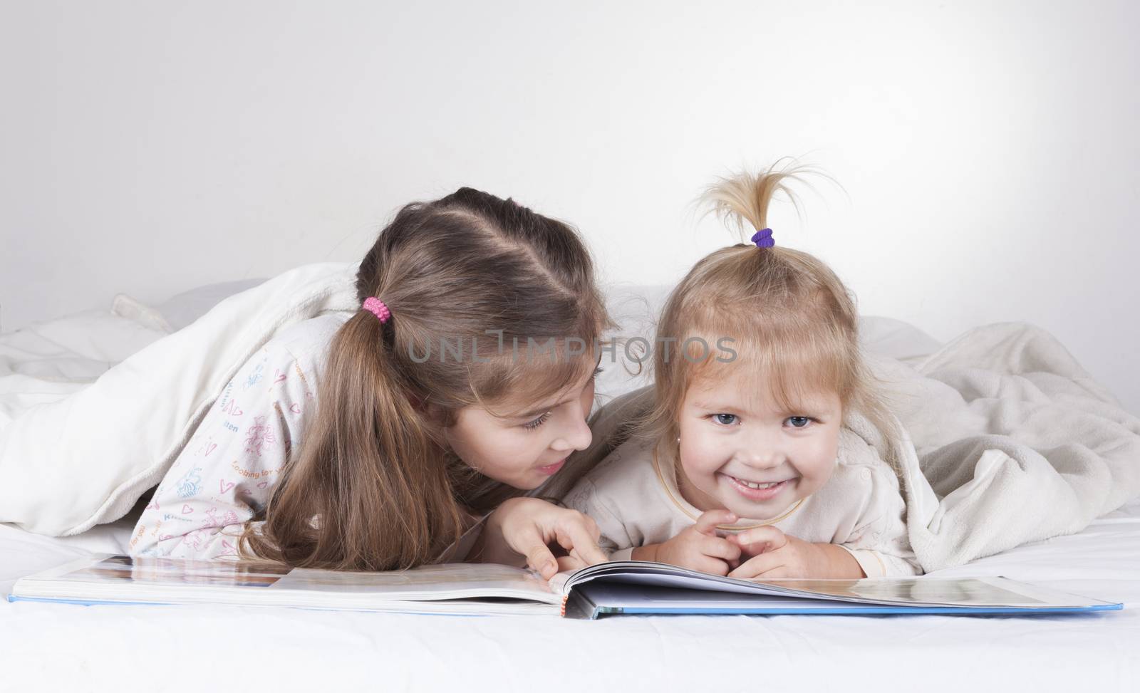 Two sisters reading bad time story in bad with white sheets