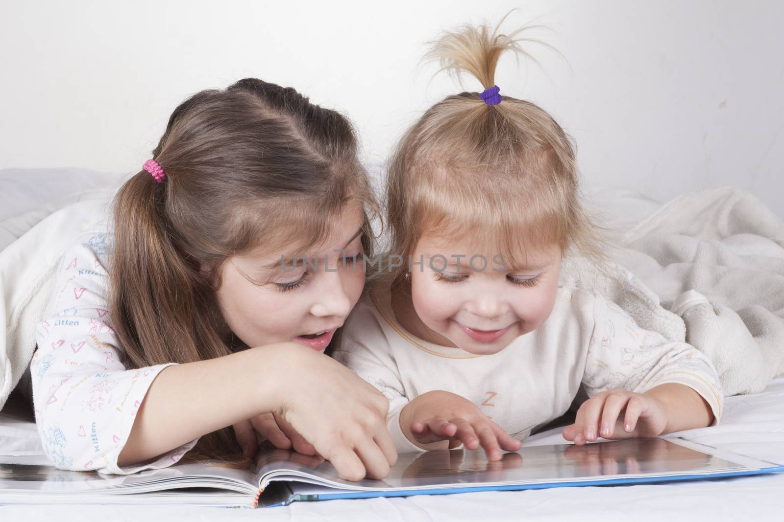 Two sisters reading bad time story in bad with white sheets