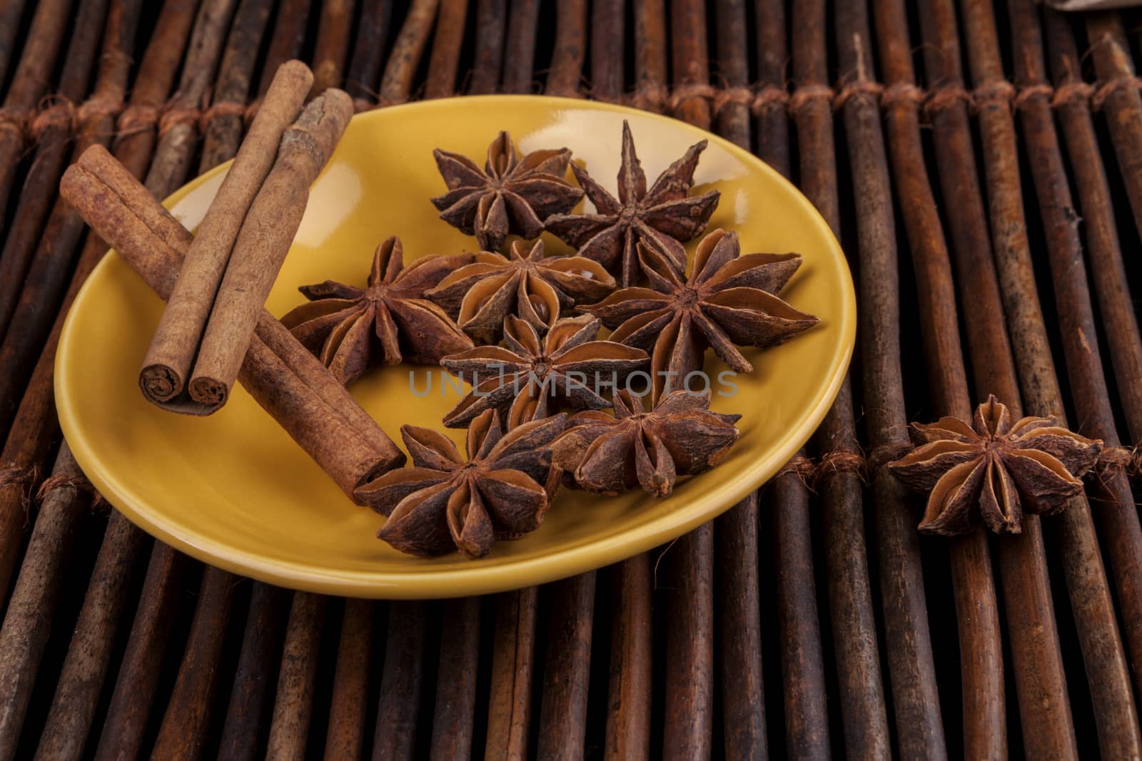 Cinnamon sticks with star shape anis on yellow plate and wood background