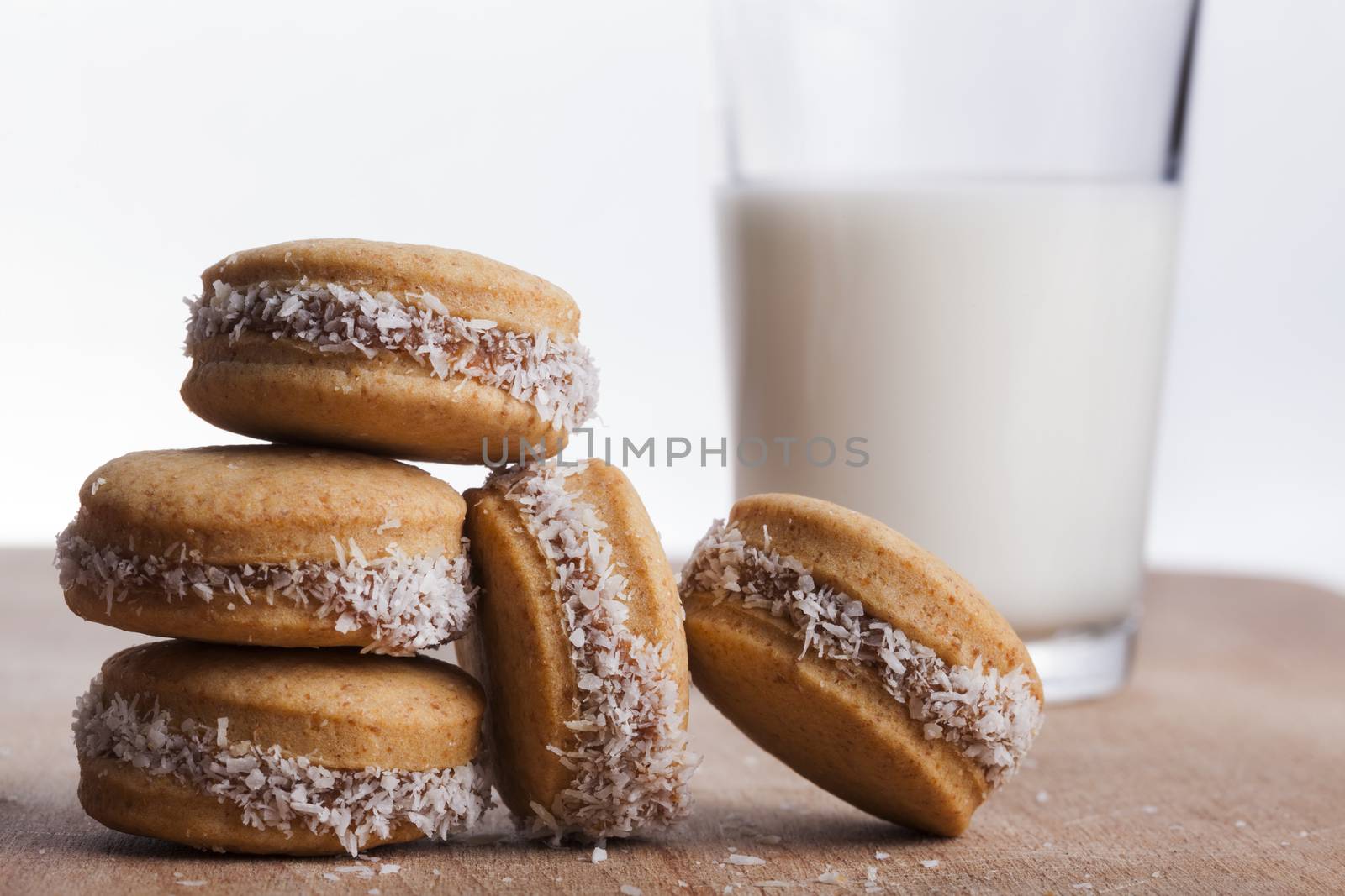 Small round cocnut cookies with  glass of milk in the bakcground on wooden plate