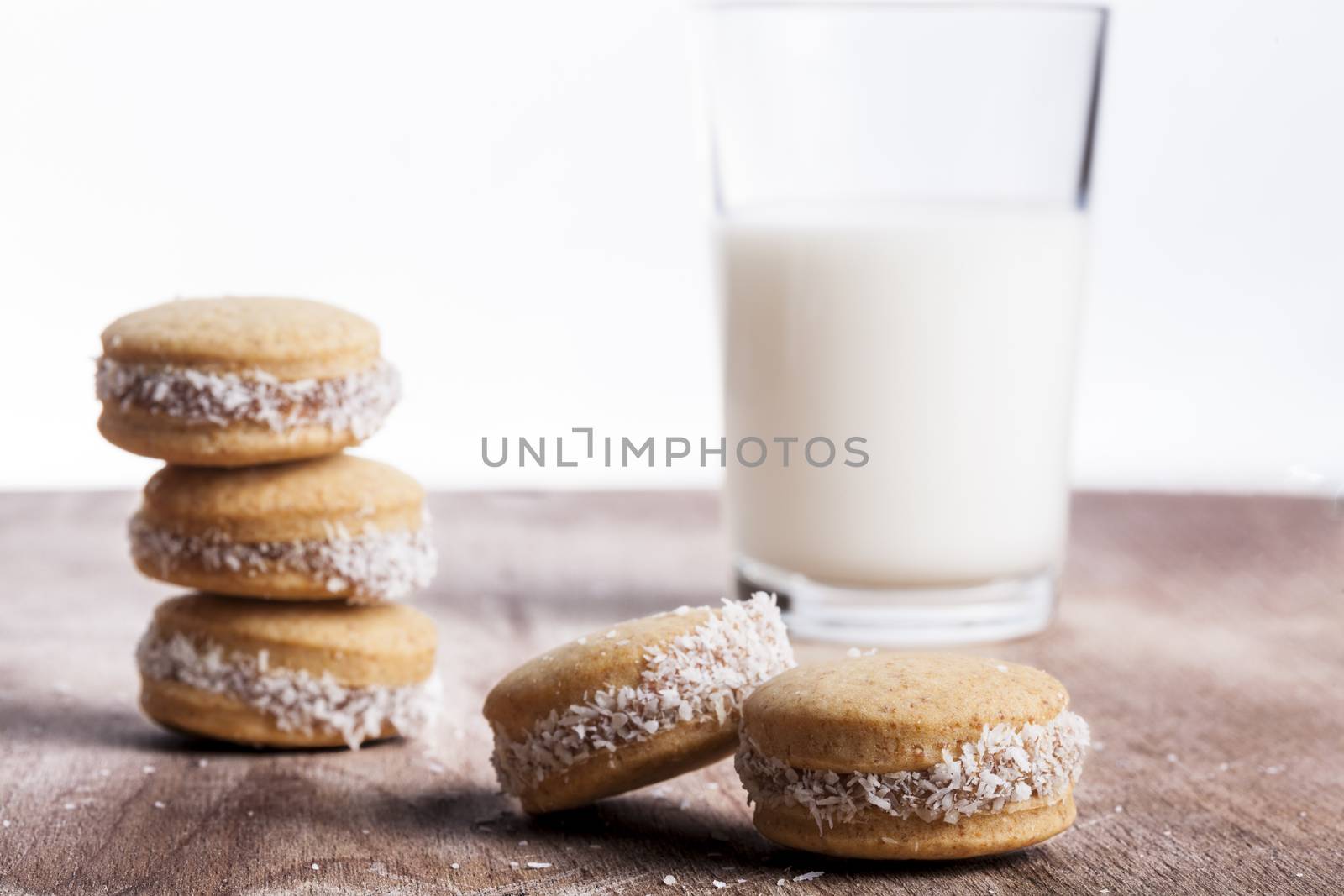 Small round cocnut cookies with milk glass in the bakcground on wooden plate