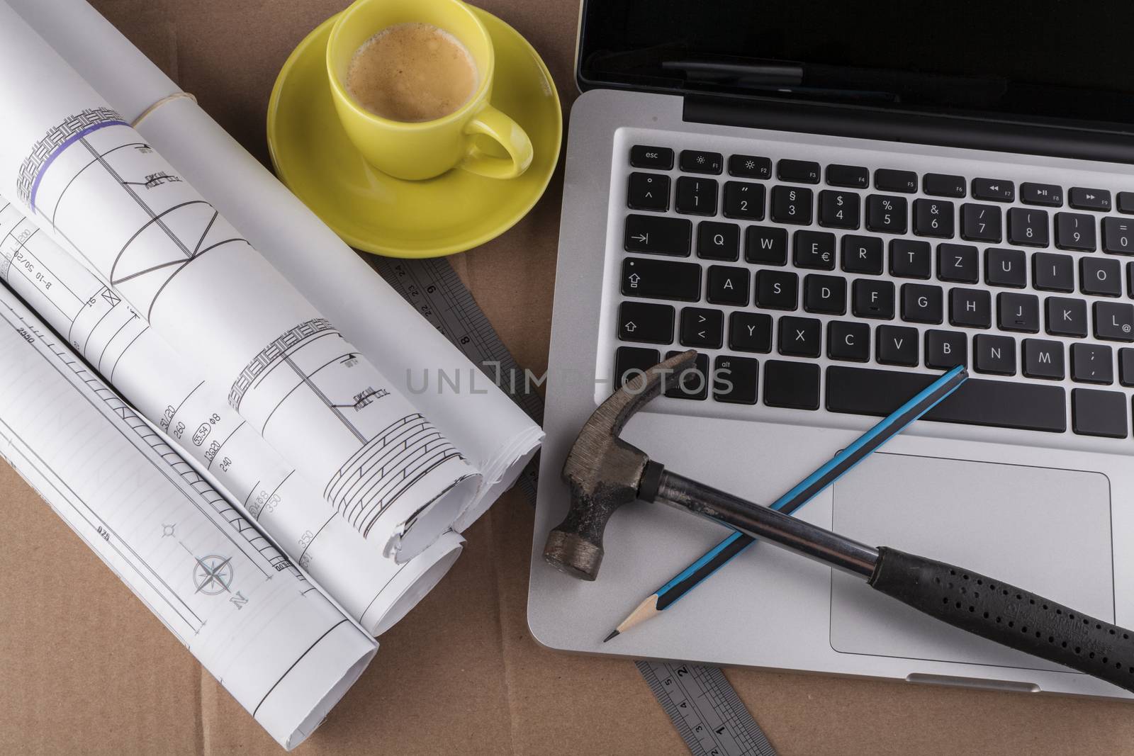 Architectural plans rolled with silver laptop hamer and a pencil