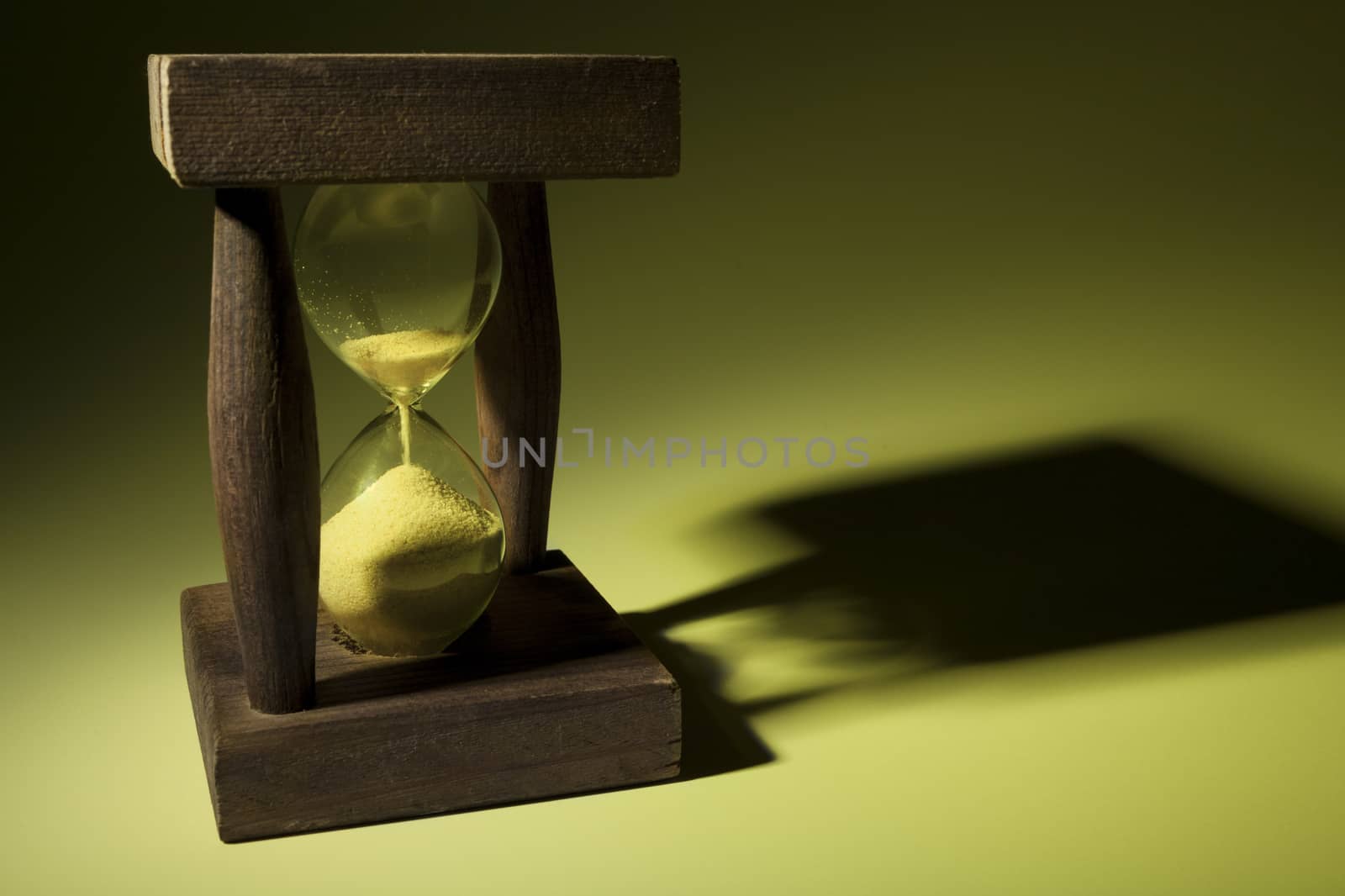 Old wooden hourglass with shadow in yellow light