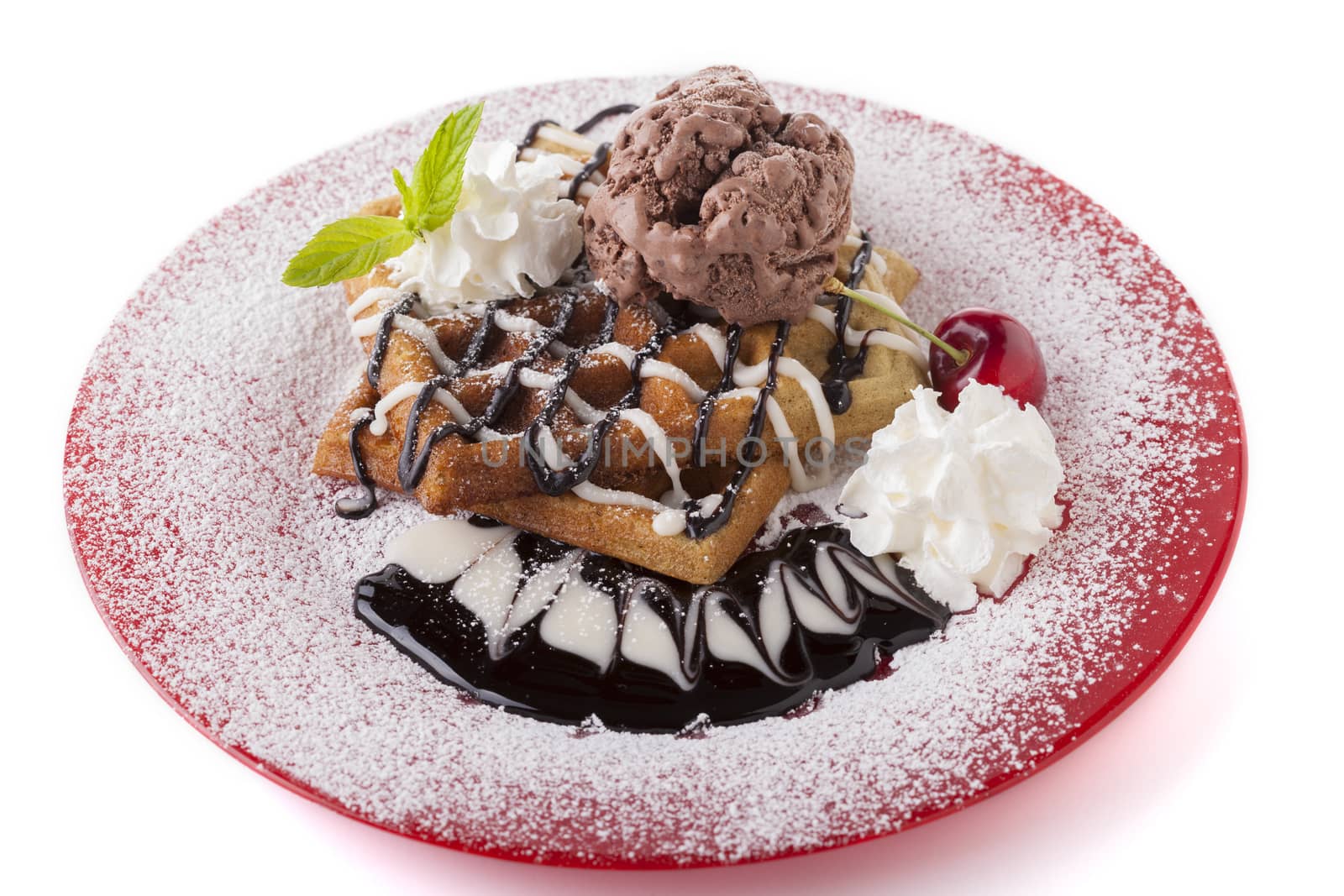 Belgian waffle with chocolate syrup whipped cream and red cherry on red plate