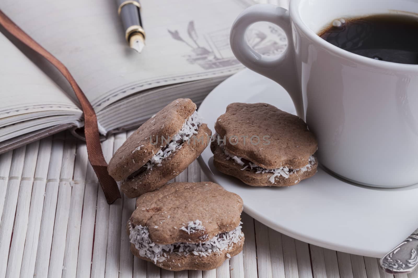 brown cookies with coffee in a white mug and silver spoon with fountainpen and old notebook on white wood background