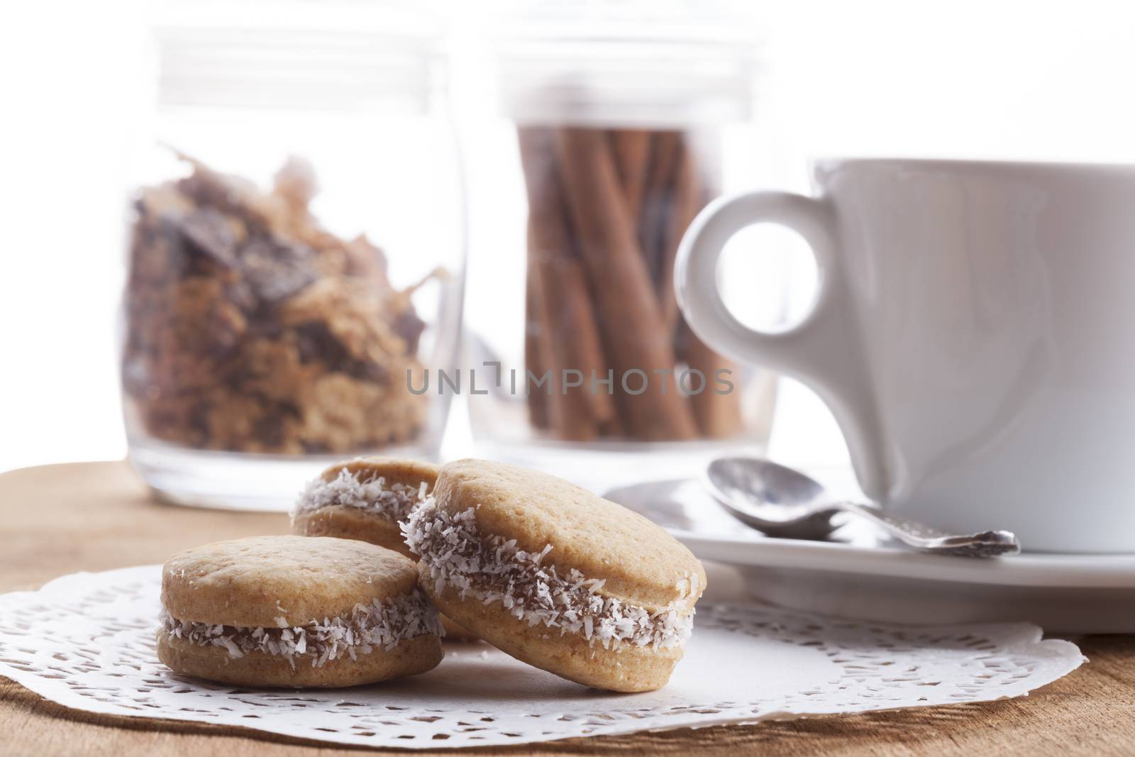 Small round cocnut cookies with white coffee mug in the bakcground on wooden plate
