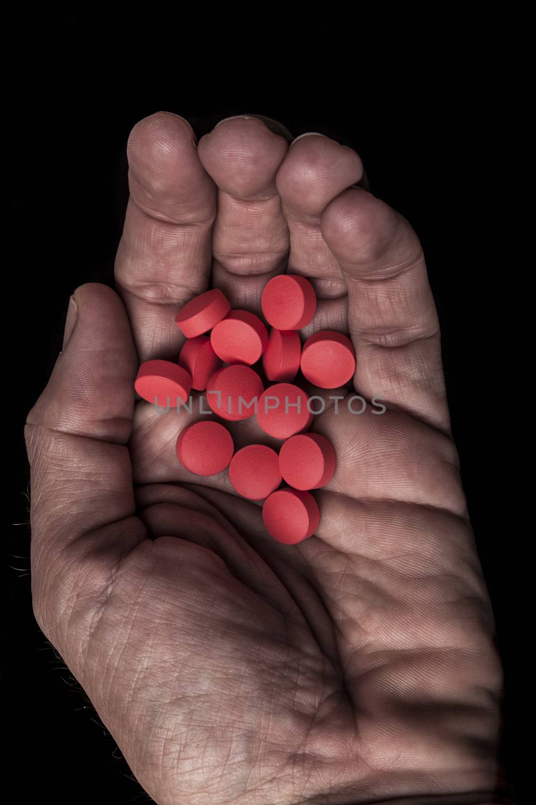 Old dirty hand with round red pills on black background