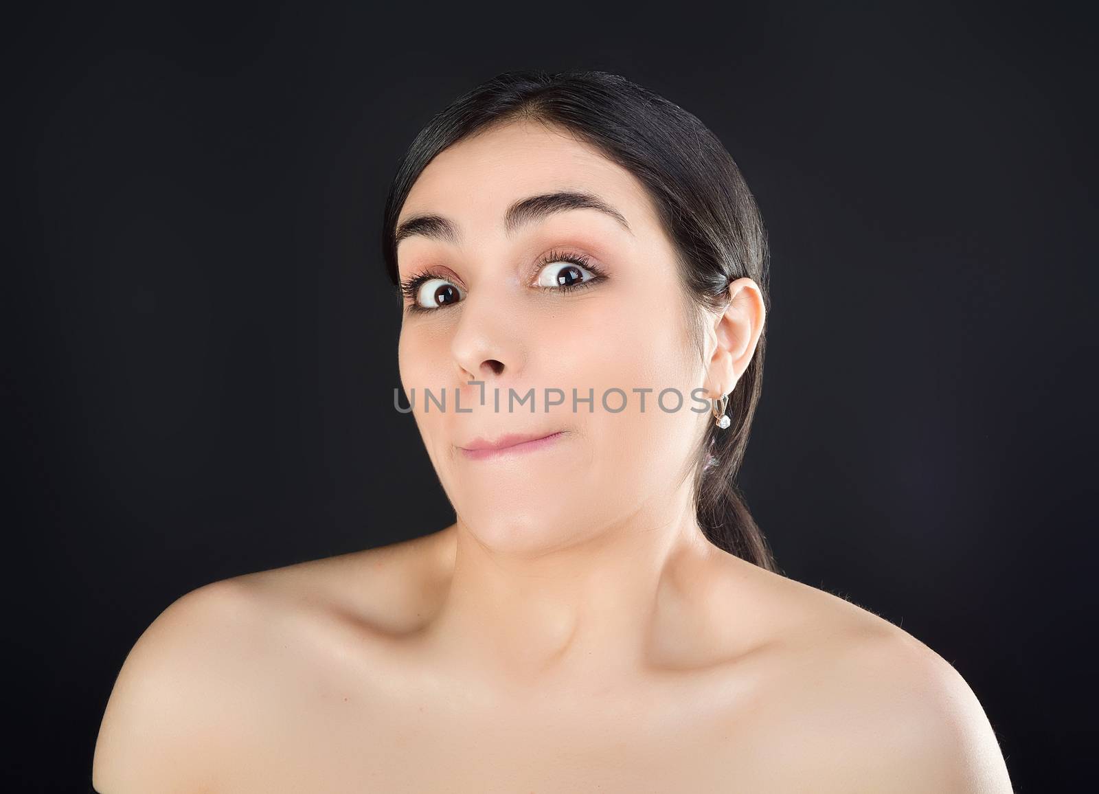 Beauty portrait of a girl with bare shoulders who is surprised at the camera. Studio shot on black background