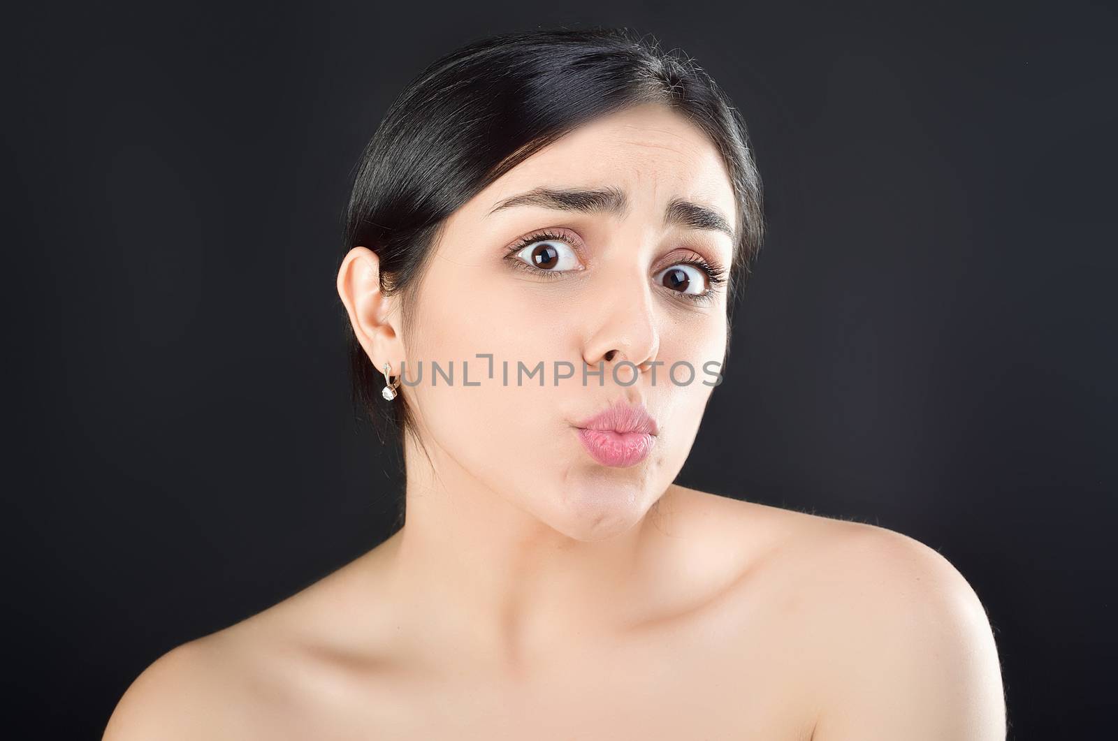 Beauty portrait of a girl with bare shoulders who shows off her lips sending a kiss to the camera. Studio shot on black background