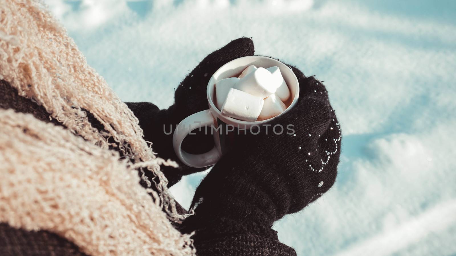A cup of cocoa with marshmallows in hands in mittens. Warm winter background. Warming drink.