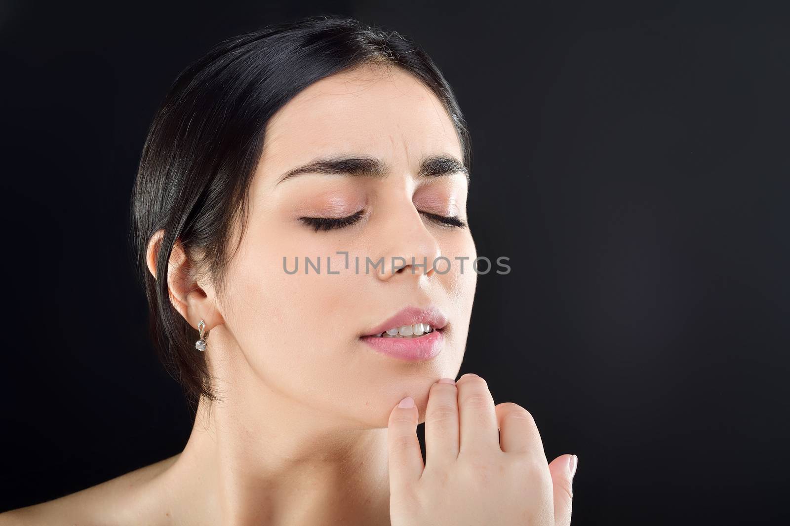 Pretty woman gently twists her fingers around her chin with her eyes closed, turning her head towards the Studio photo, black background