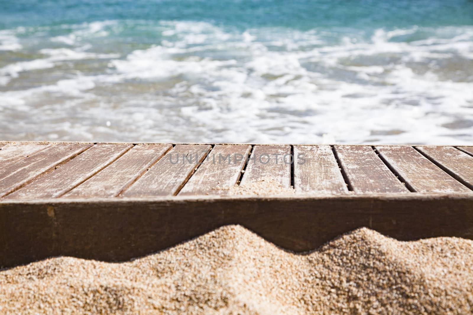 wooden plank in sand and blue sea in the background