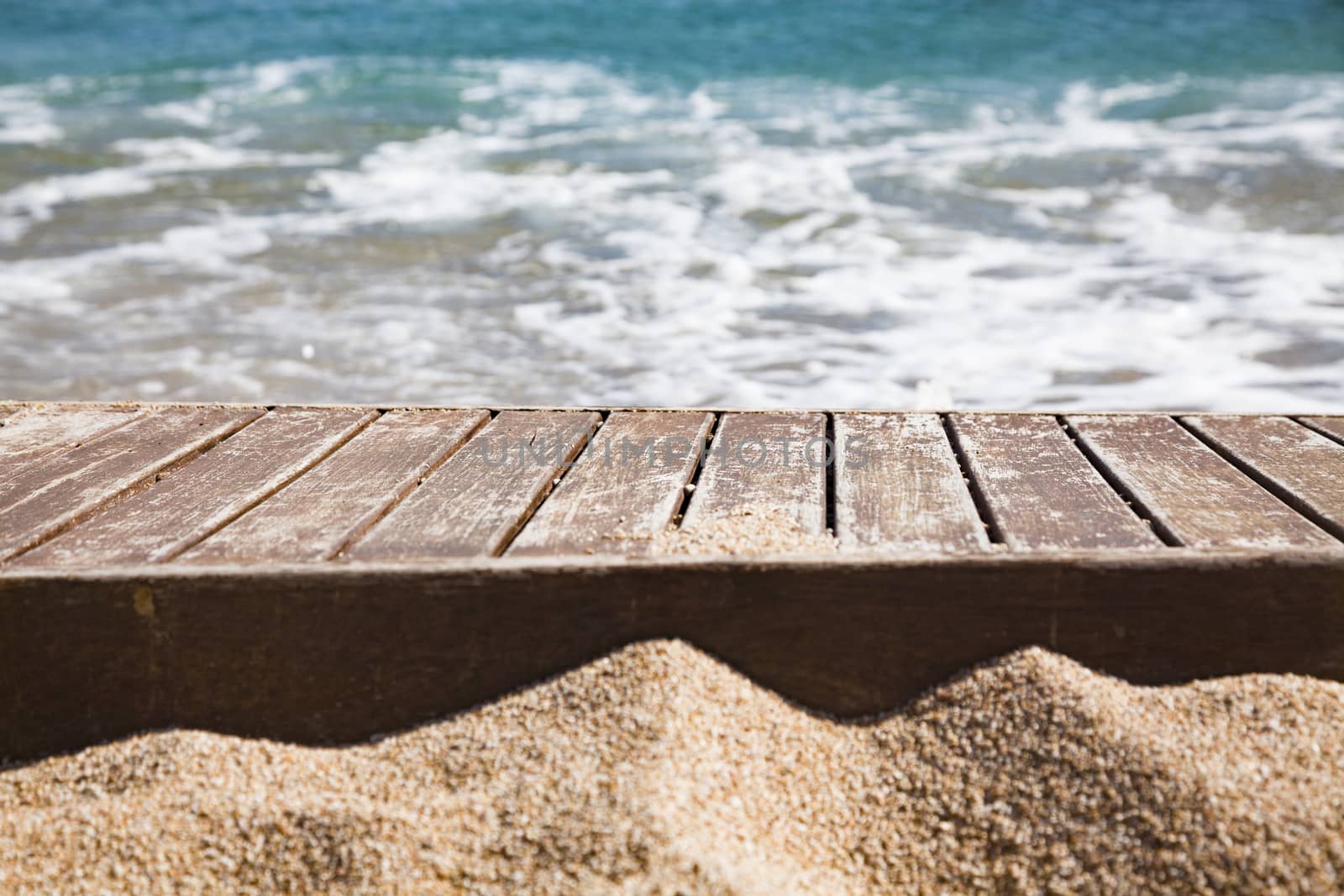 wooden plank in sand and blue sea in the background