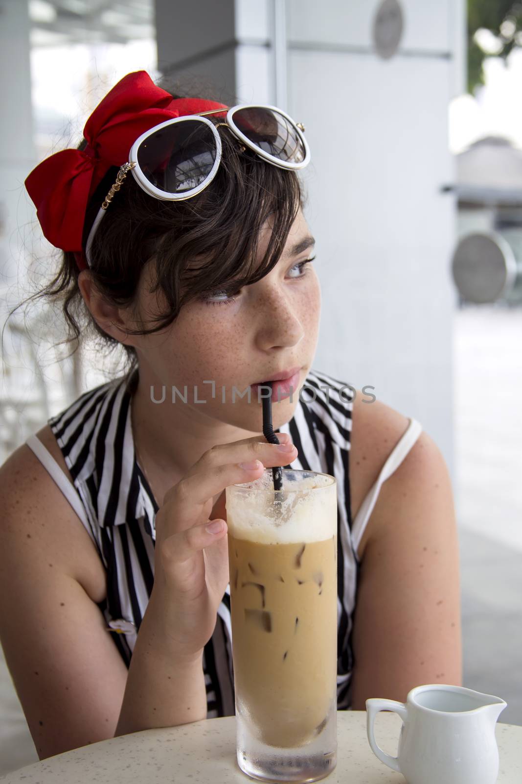 A teenage girl drinks ice coffee through in a cafe by Anelik