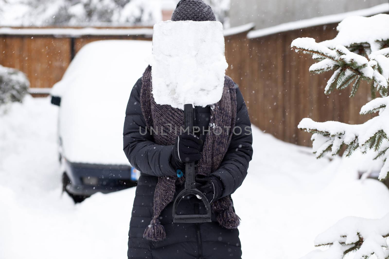 woman with shovel cleaning snow aeound car. Winter shoveling. Removing snow after blizzard