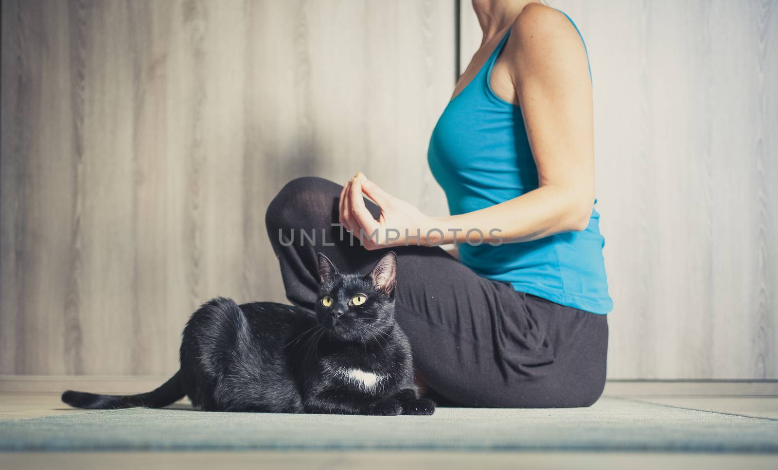 woman doing yoga at home - black cat sitting next to her