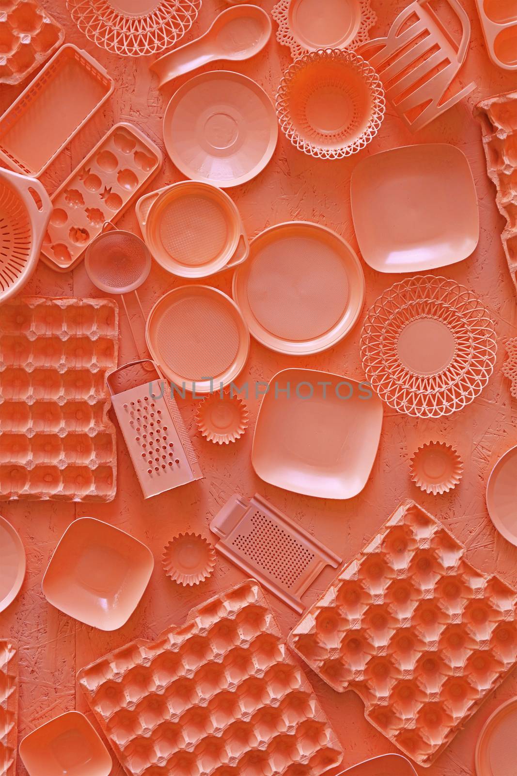 Close up flat lay of different orange color painted kitchen utensils and tools, grater, spoon, egg carton, plastic disposable plates, elevated top view, directly above