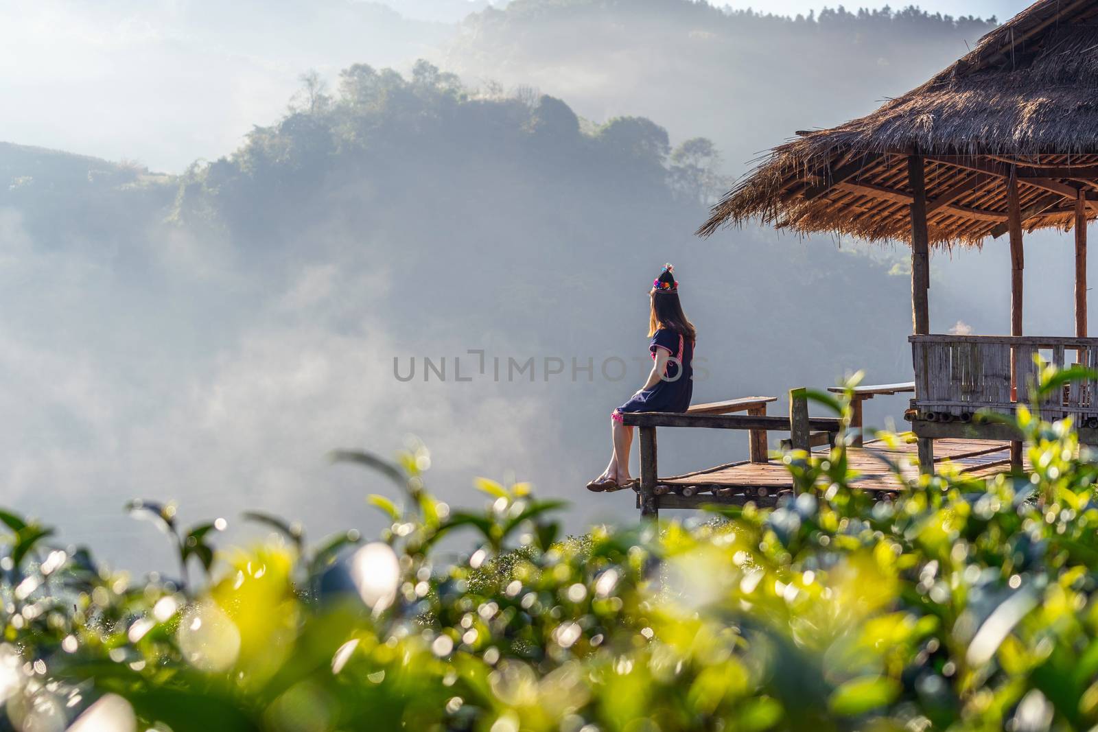 Woman wearing hill tribe dress sitting on the hut in green tea field. by gutarphotoghaphy