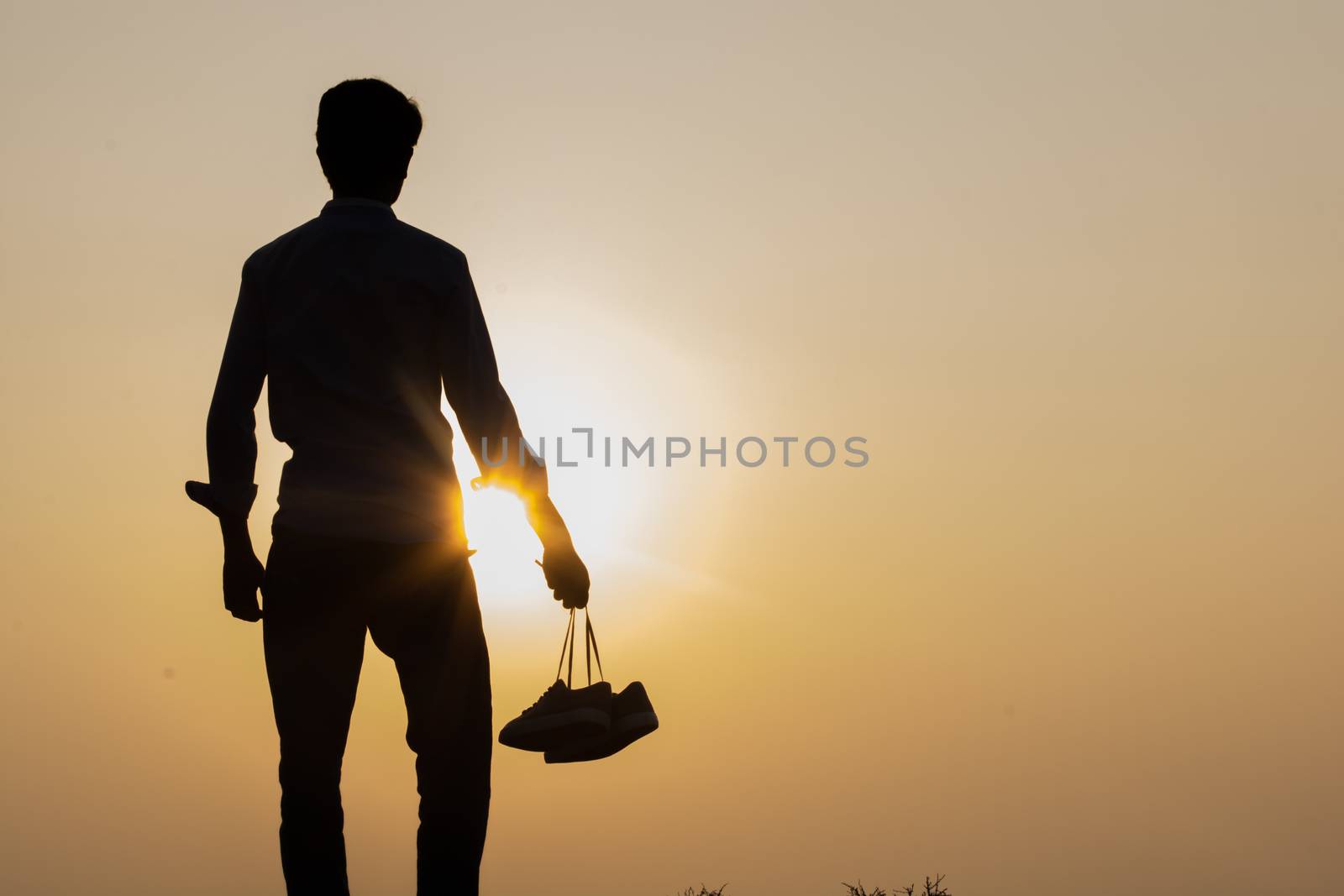 The Boy standing at sunset and holding shoes in his hand Close-up