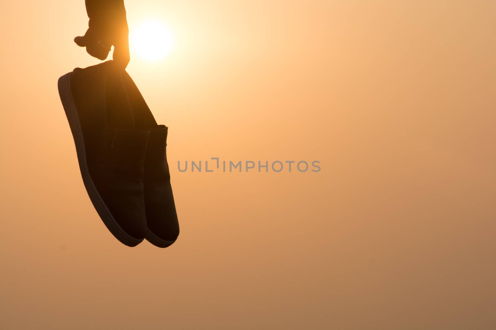 The Boy standing at sunset and holding shoes in his hand Close-up