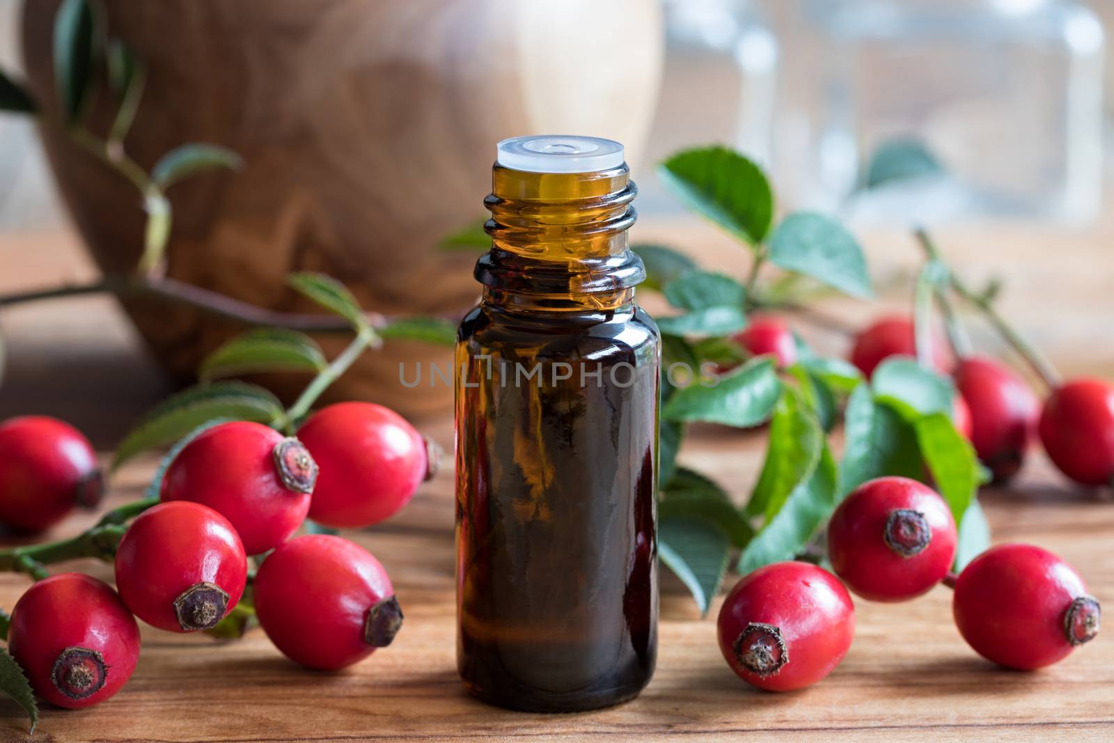 A bottle of rosehip seed oil on a wooden table, with fresh rosehips in the background