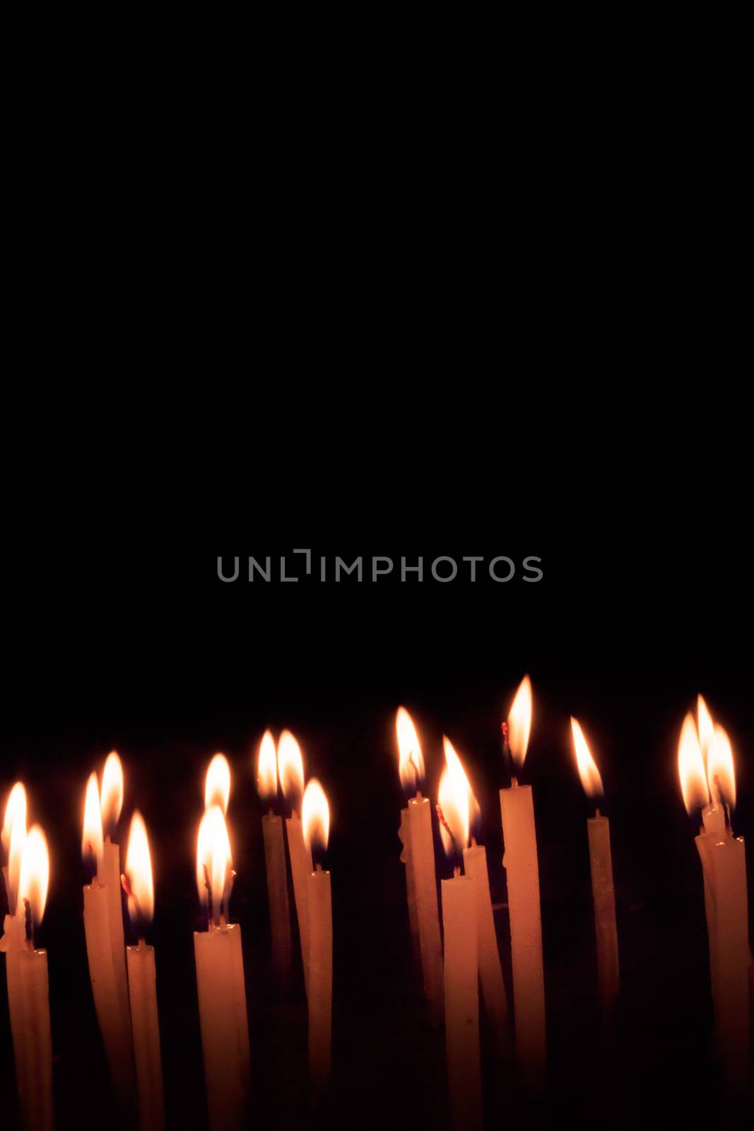 Many christmas candles burning at night on the black background. Candle flame set isolated in black background. Group of burning candles in dark with shallow depth of field. Close-up. Free space.