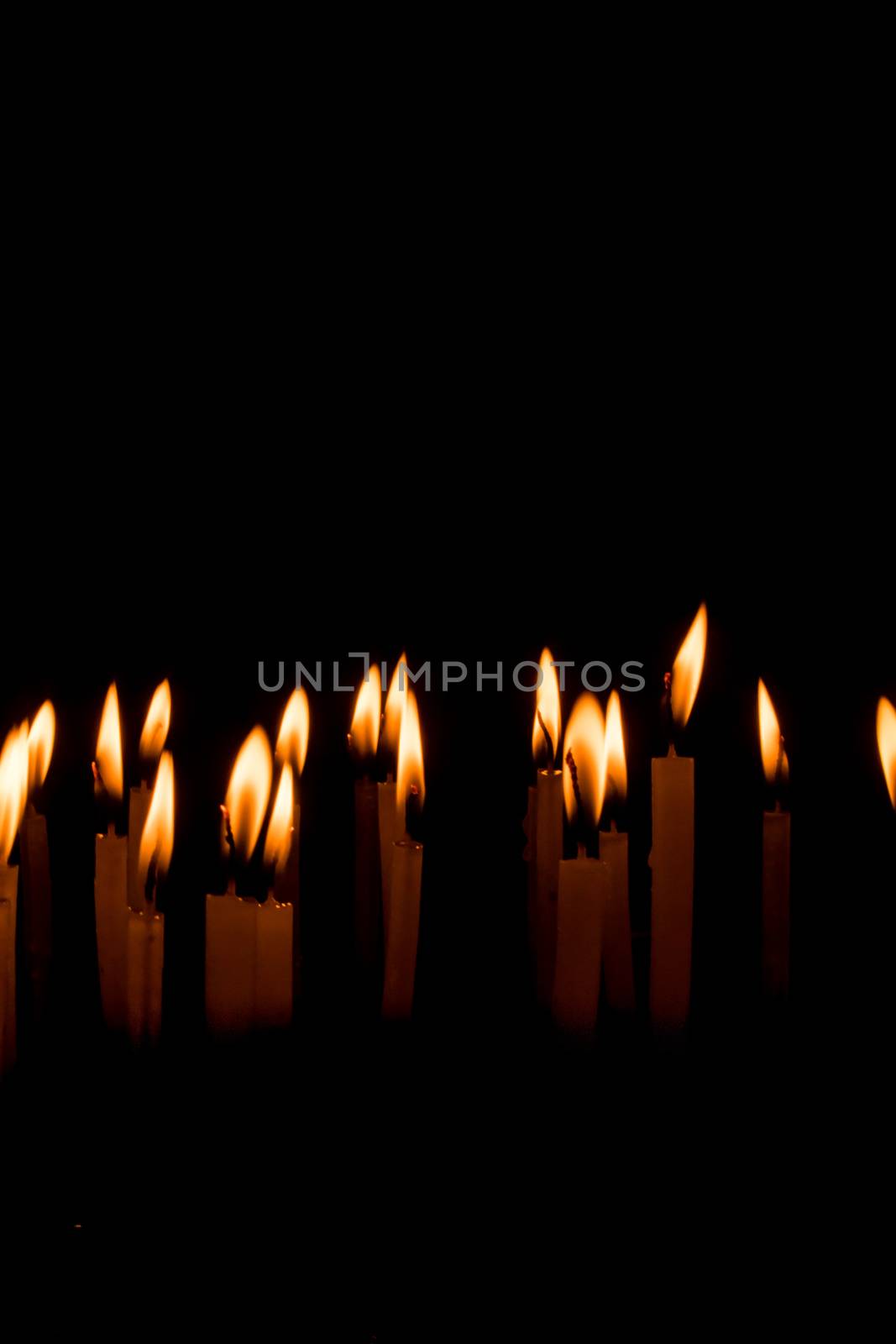 Many christmas candles burning at night on the black background. Candle flame set isolated in black background. Group of burning candles in dark with shallow depth of field. Close-up. Free space.