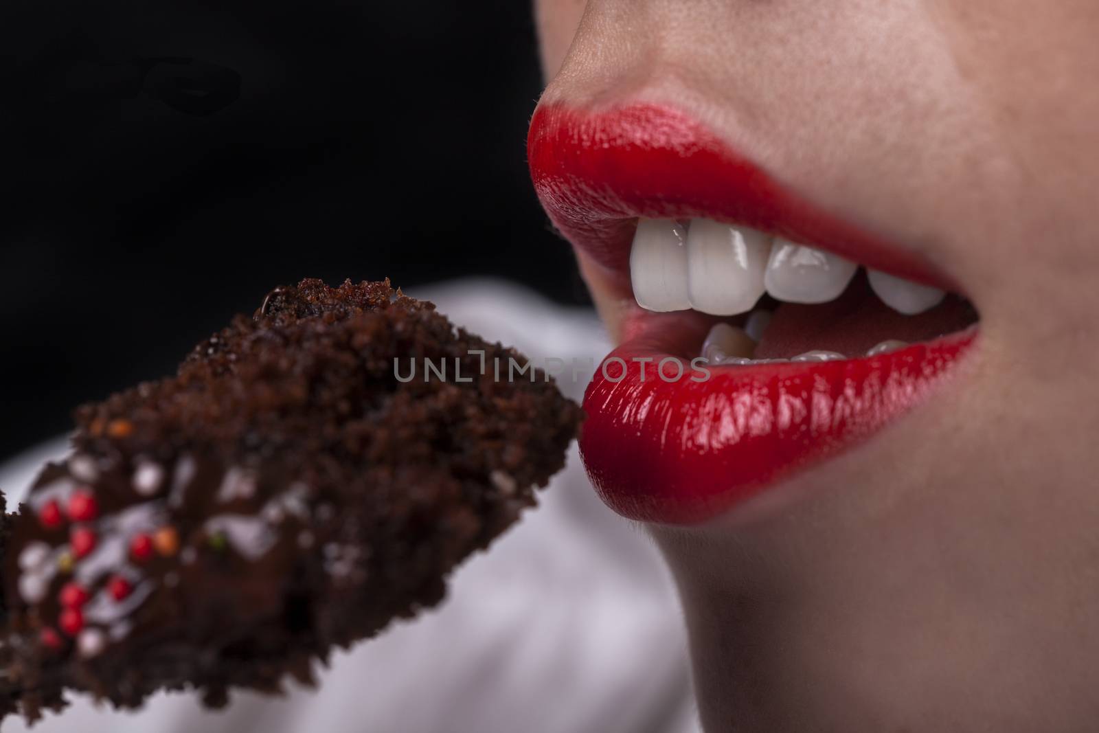 Young girl mouth with red lips eating chocolate cake