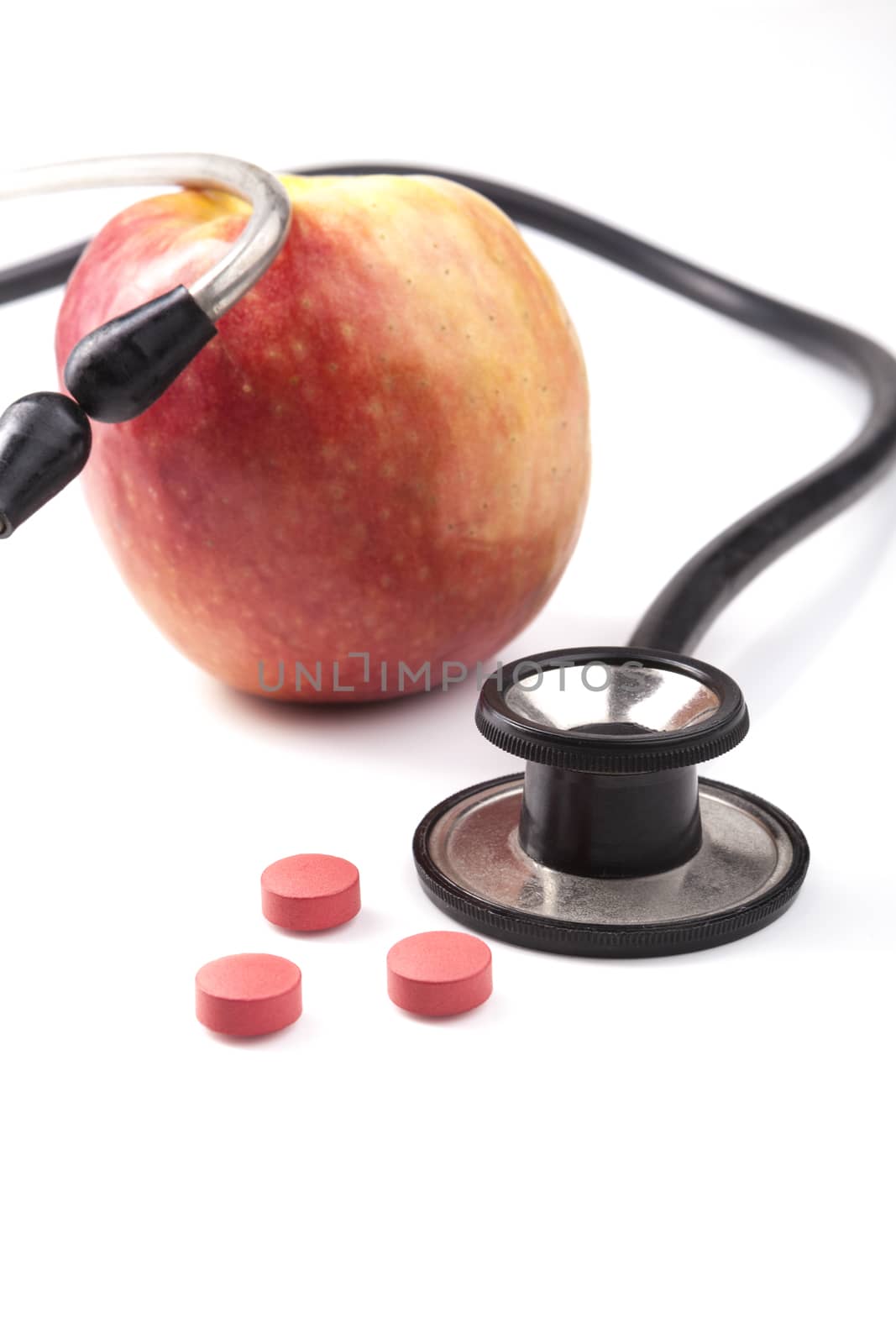 Red Apple with black stethoscope and red pills with reflection isolated on white background