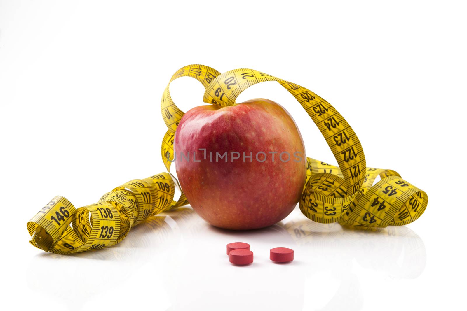 Red Apple with yellow measuring tape and red pills with reflection isolated on white background