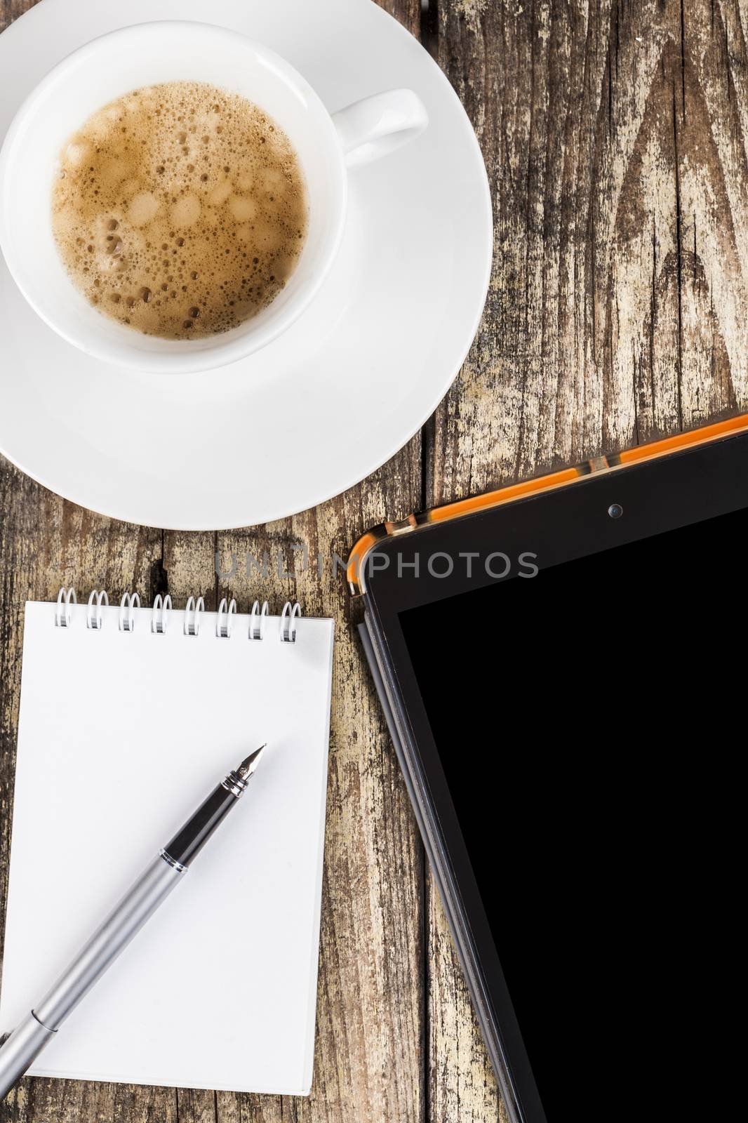 Morning coffee with a spiral notepad and fountain-pen and a tablet on old brown dood background