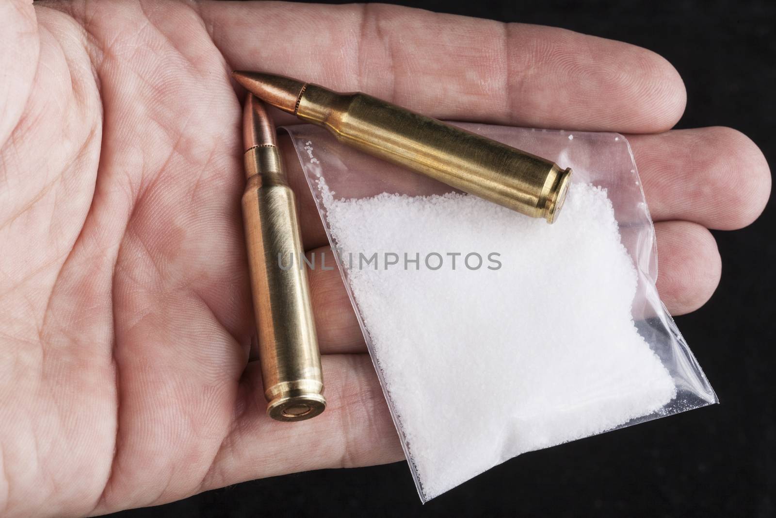 Rifle bullets close-up  in hand on black background with a bag of white drug powder