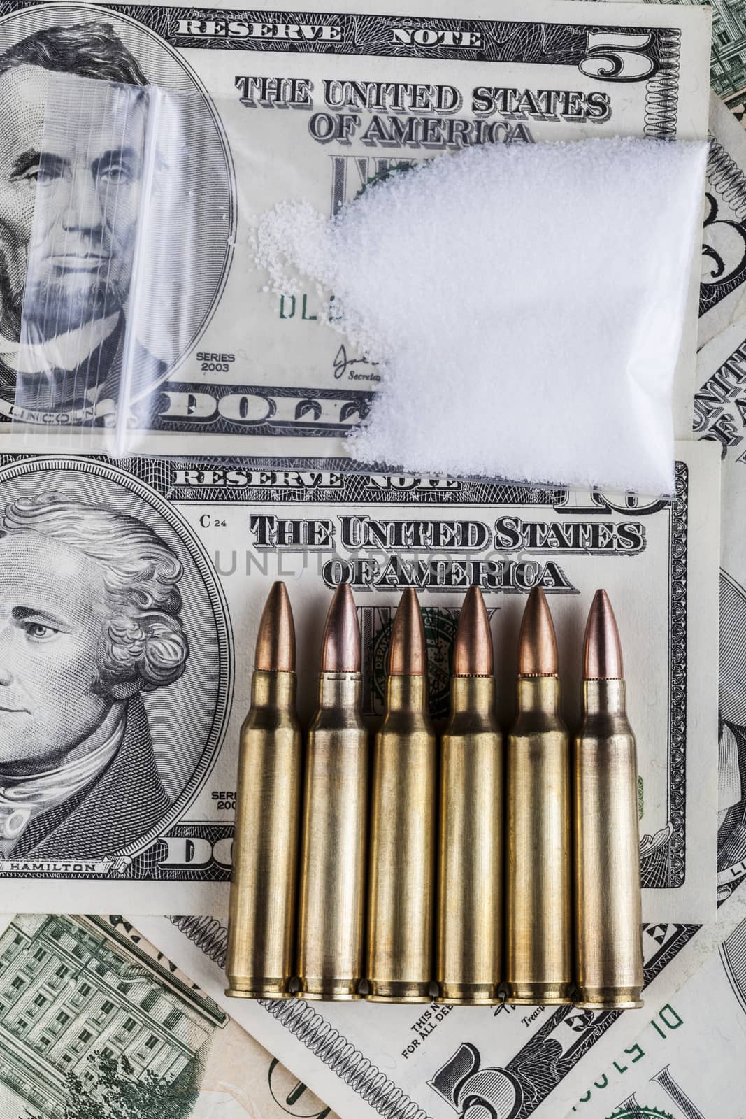 Bullets on dollar banknotes with bag of white drug powder on black background