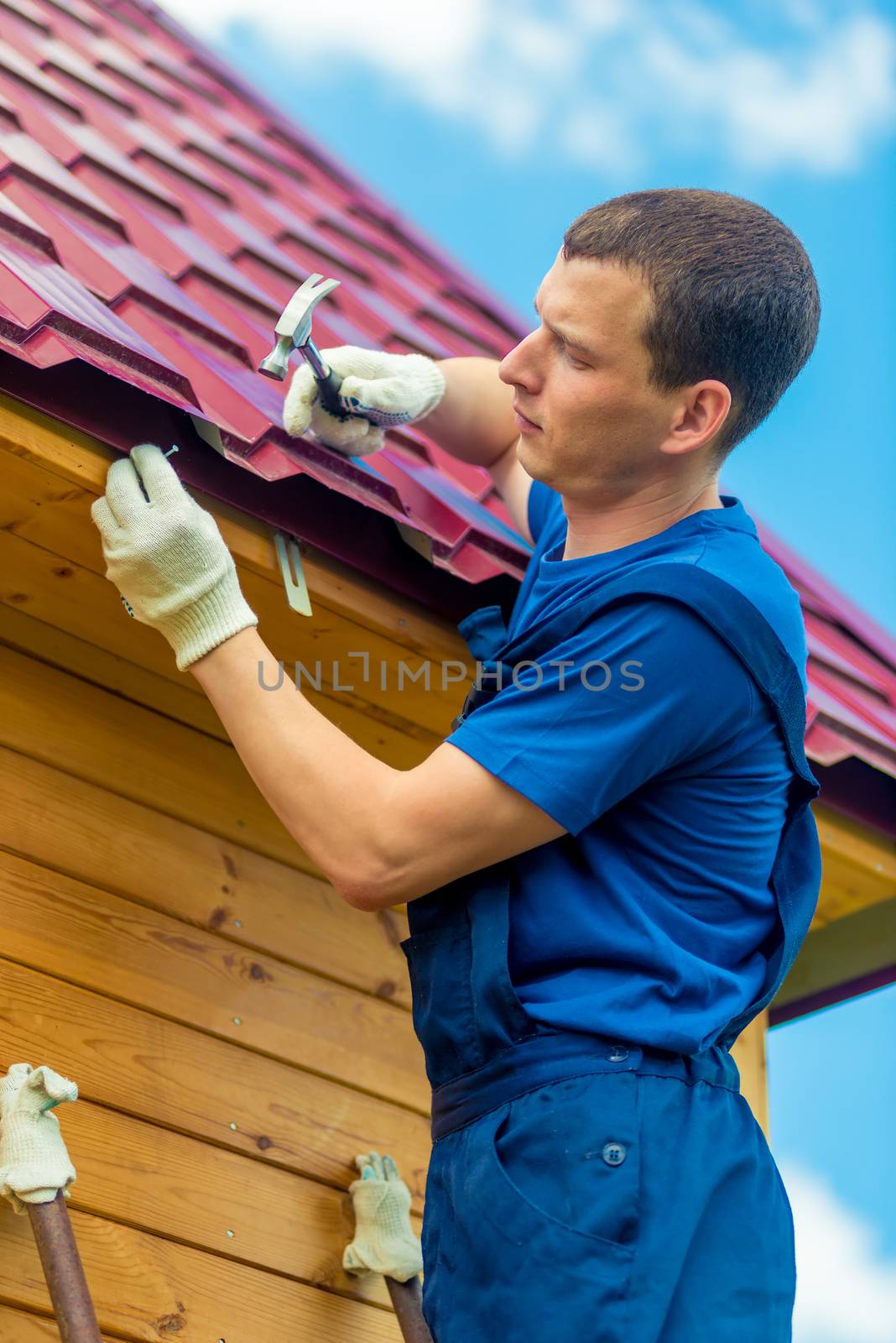 A man with a hammer and a nail repairs the roof of a house, shoo by kosmsos111