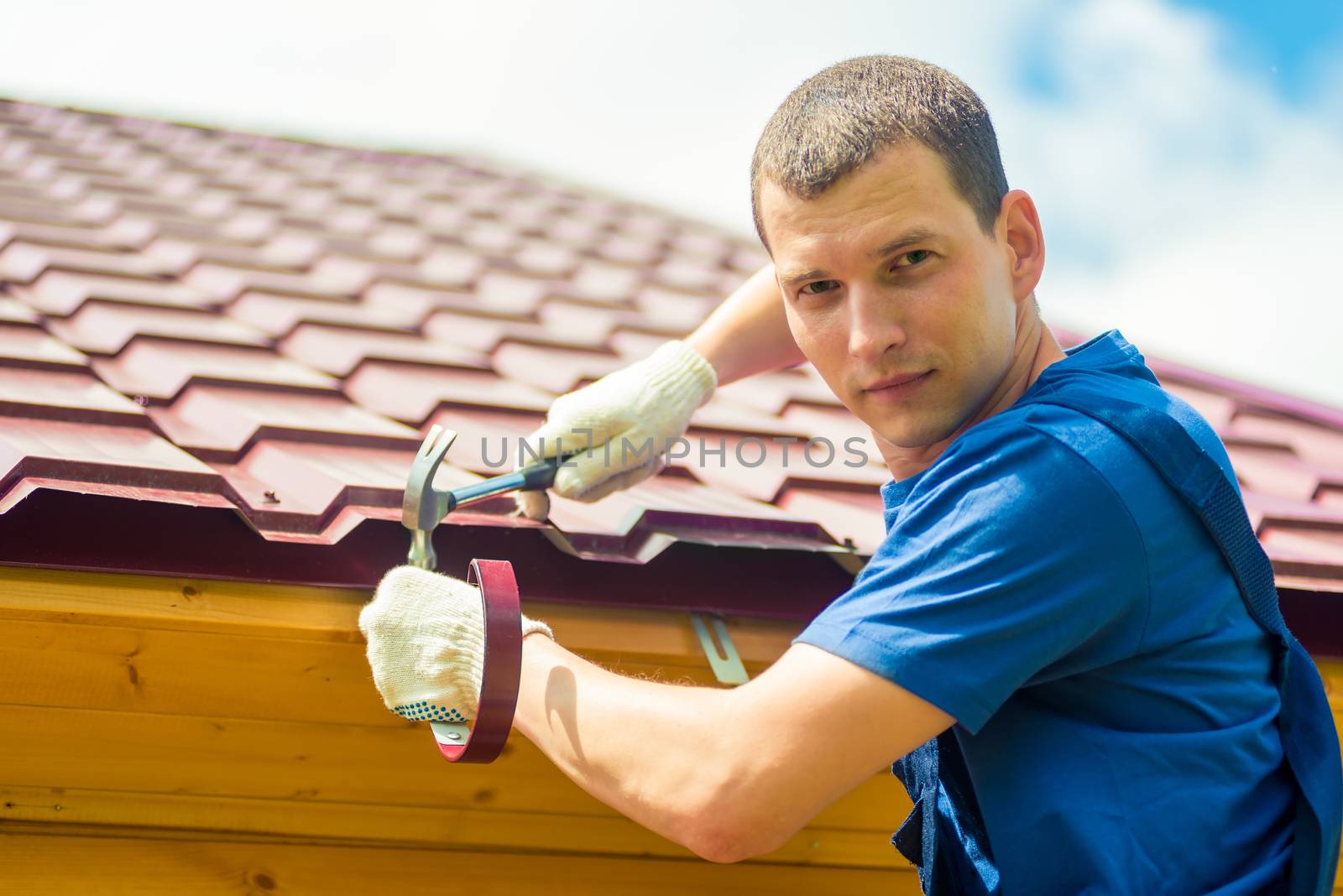 Portrait of a male repairman engaged in repairing a roof of a house, a portrait against a tile
