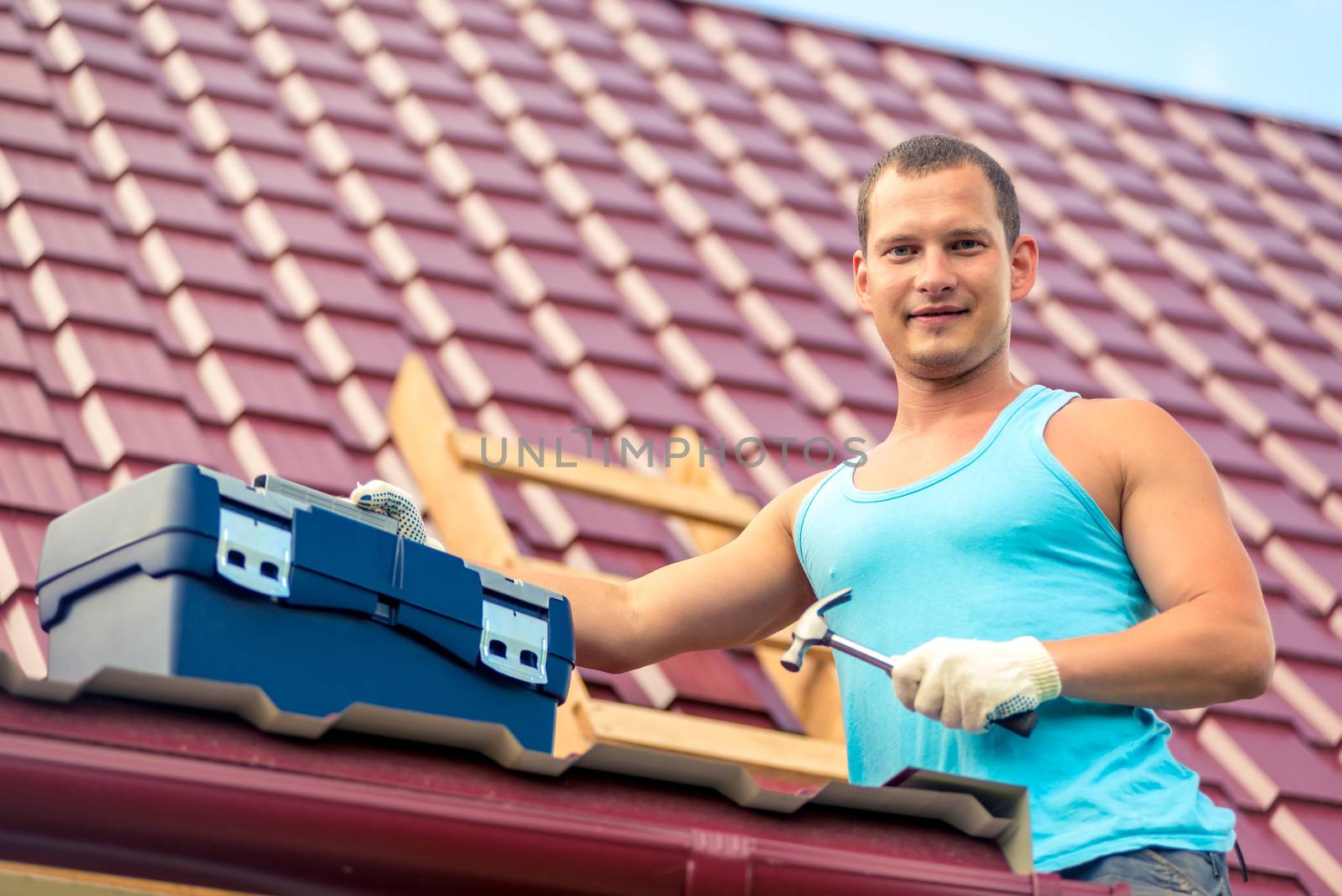 portrait of a man with a toolbox on the roof of the house during repair on the background of roof tiles