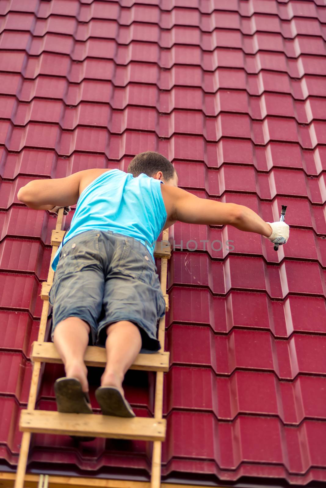 A man on the stairs with a hammer repairs the roof covering the house