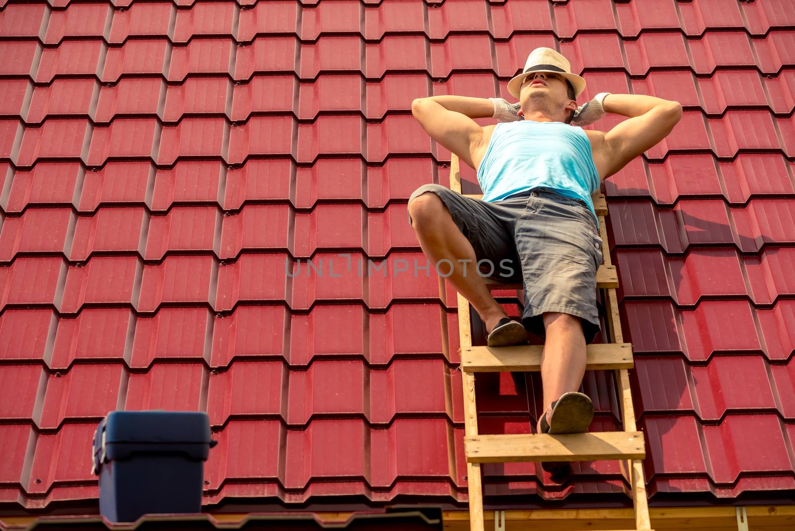 worker resting in the sun on the stairs on the roof of the house, against the background of tiles
