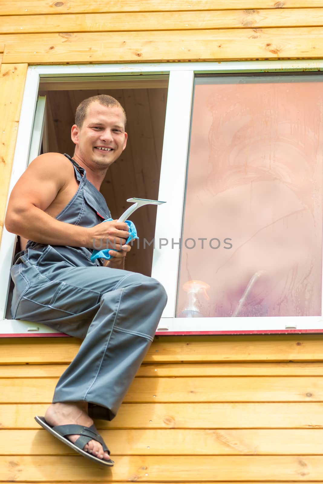 Male professional in overalls cleans the window in the house by kosmsos111